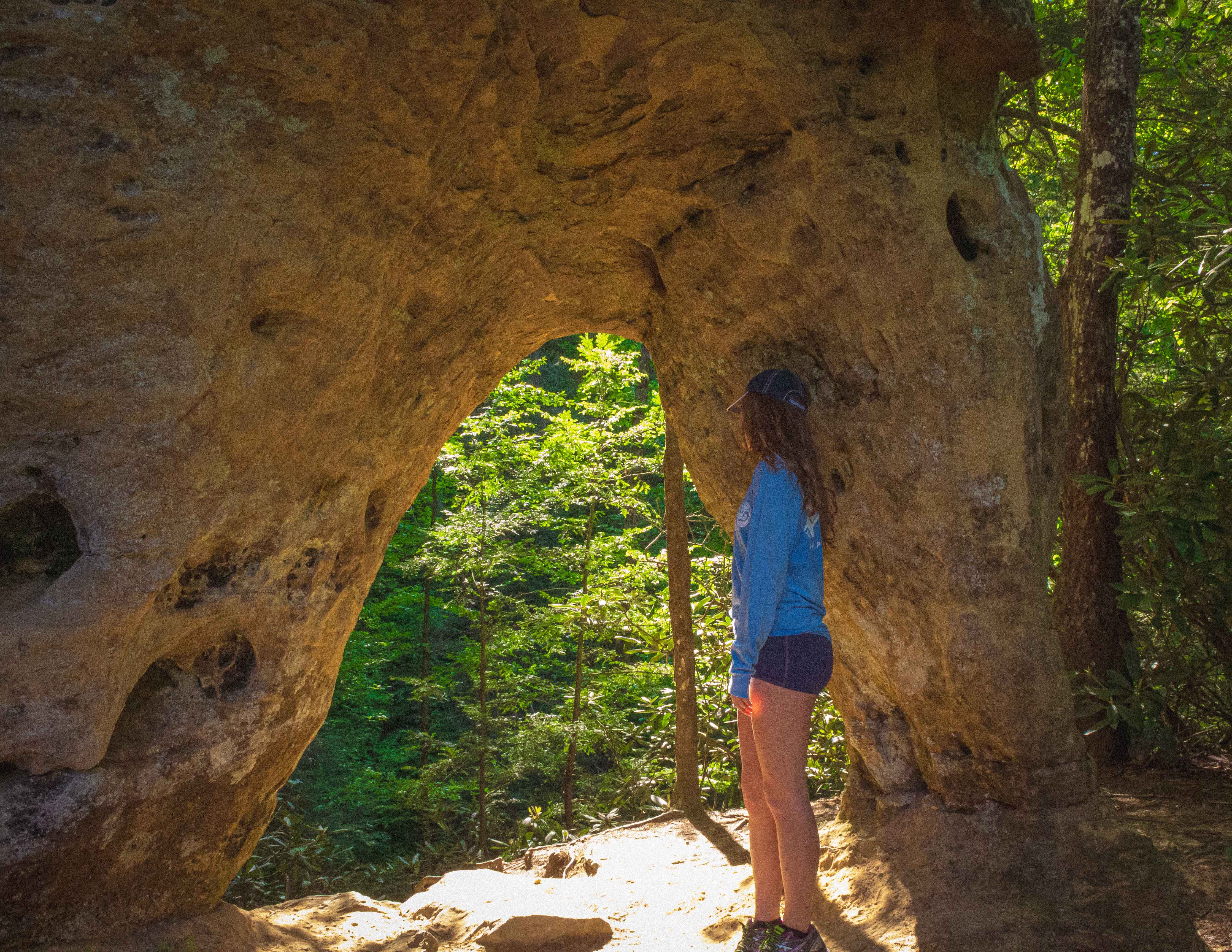 a hiker stands in front of angel's windows in the red river gorge, ky
