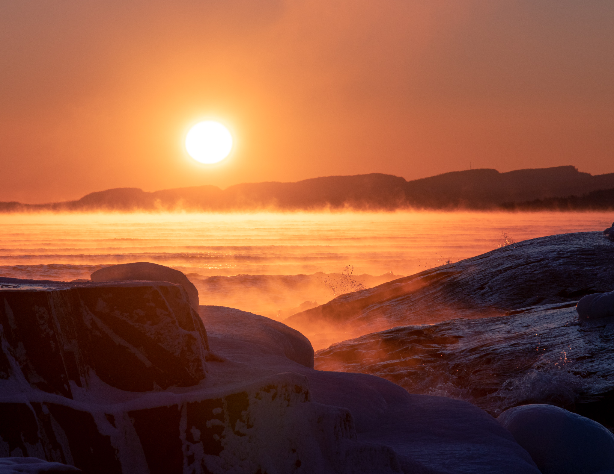 sea smoke over Lake Superior lights up orange in a setting sun