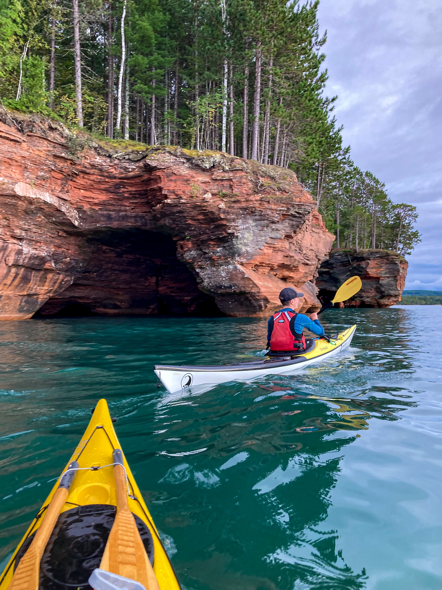 Image of the front of a sea kayak and one sea kayaker on Lake Superior under the cliffs at the Apostle Islands Sea Caves