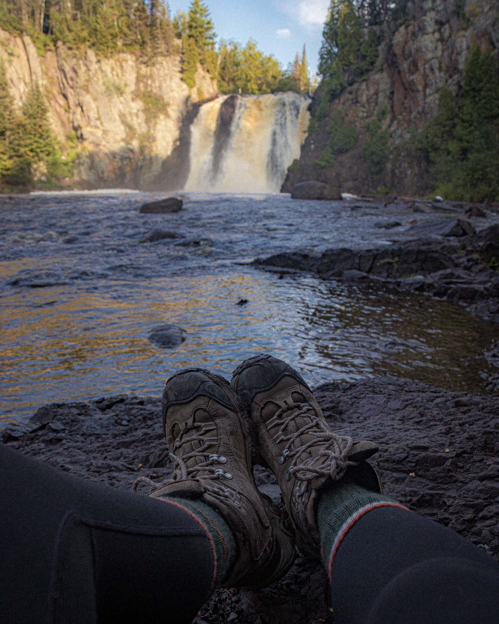 image of hiking boots in front of sunlit high falls in Tettegouche state park