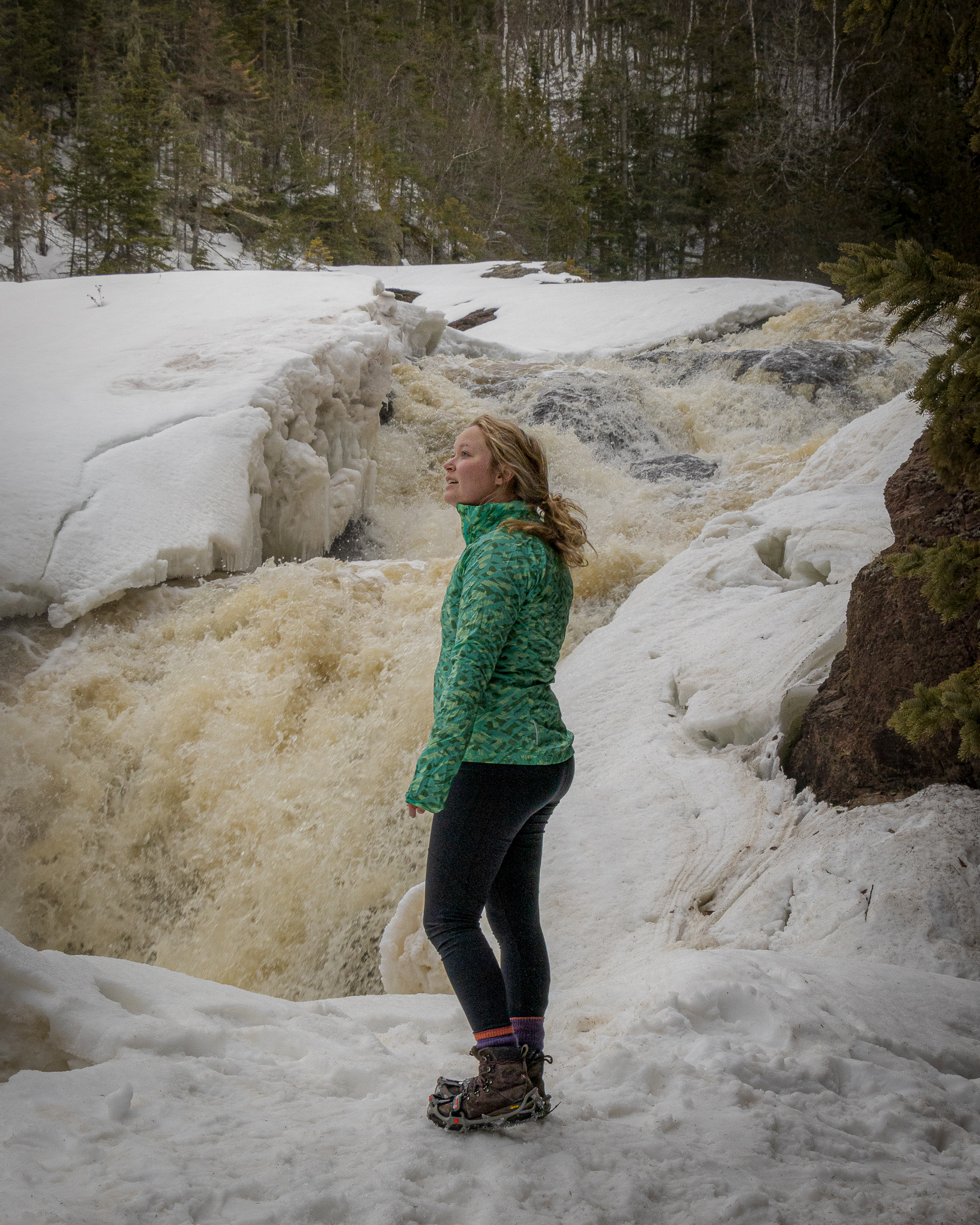 A hiker stands in front of a partially-frozen waterfall