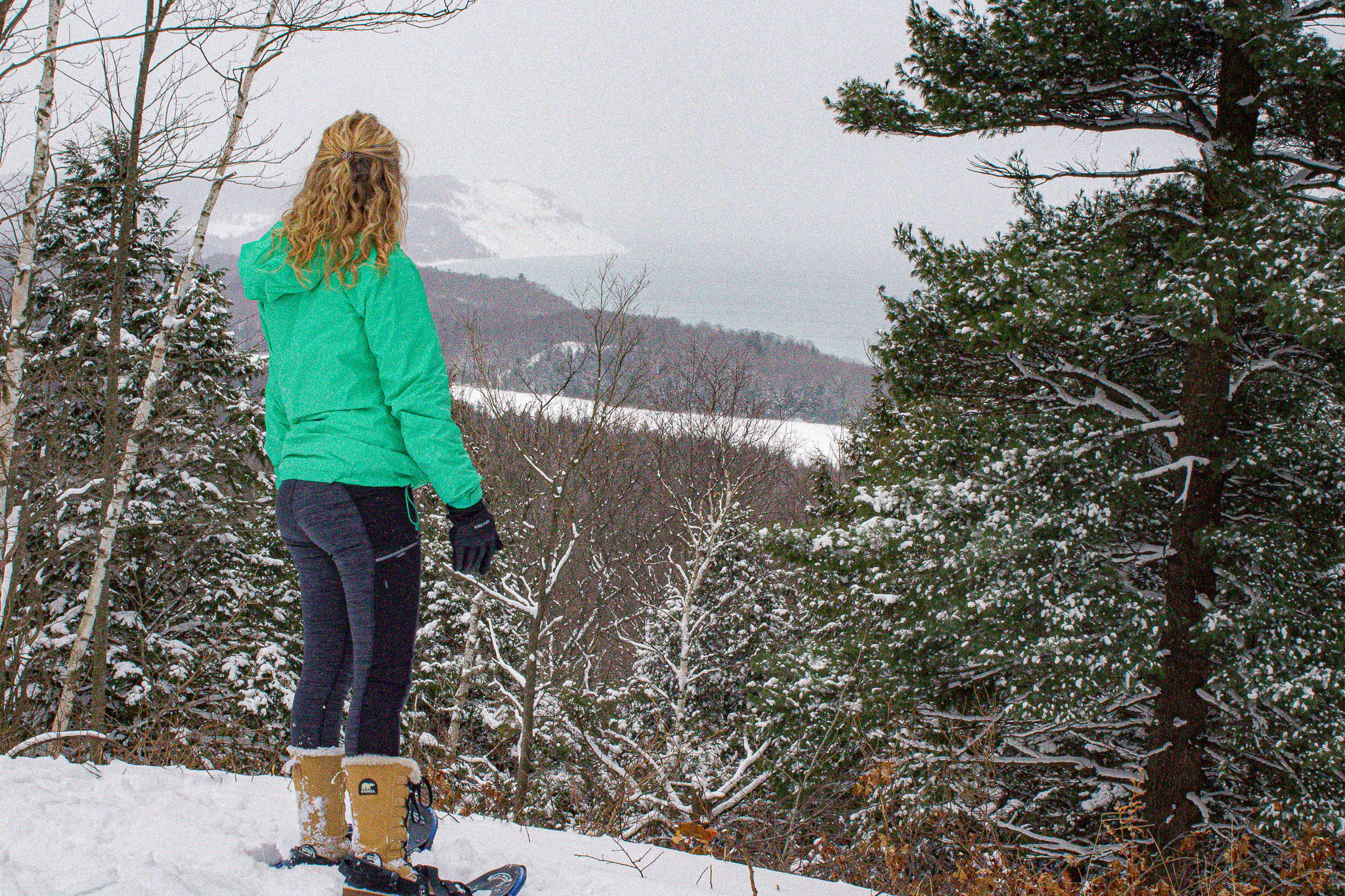 a hiker in snowshoes looks out over a snowy overlook in the Sleeping Bear Dunes National Lakeshore