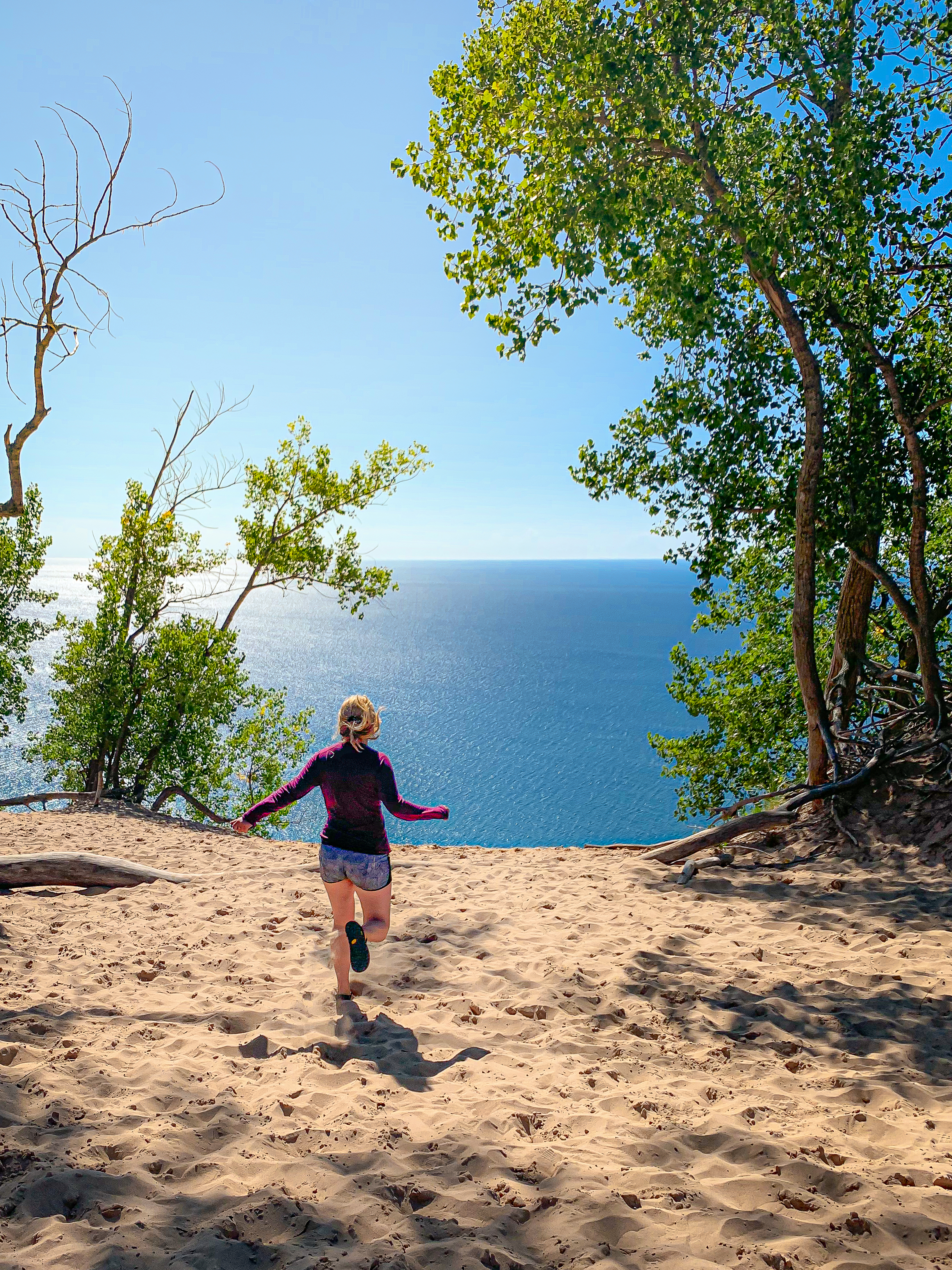 a hiker runs over the dunes out to a blue Lake Michigan