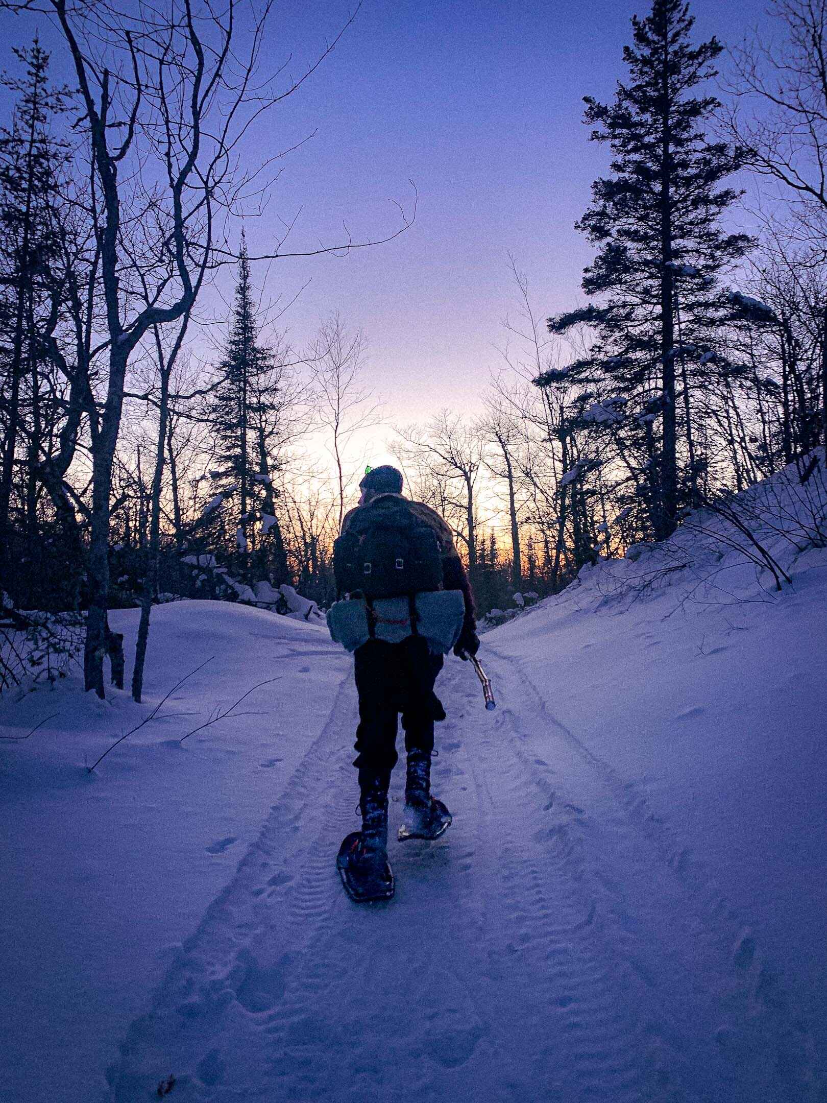 A man snowshoes up a hill at sunset