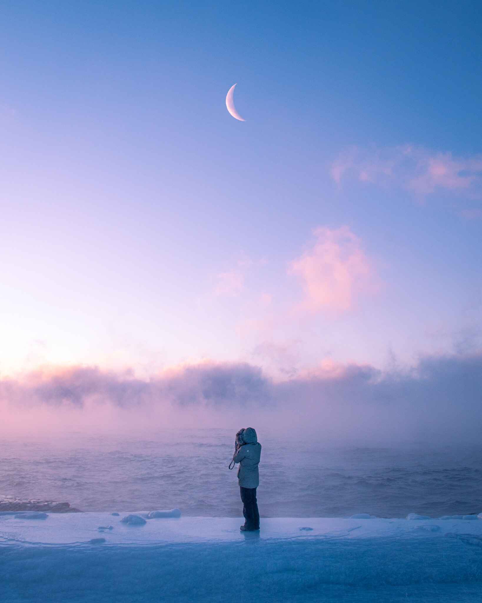A winter hiker stands on ice overlooking a sunrise on Lake Superior