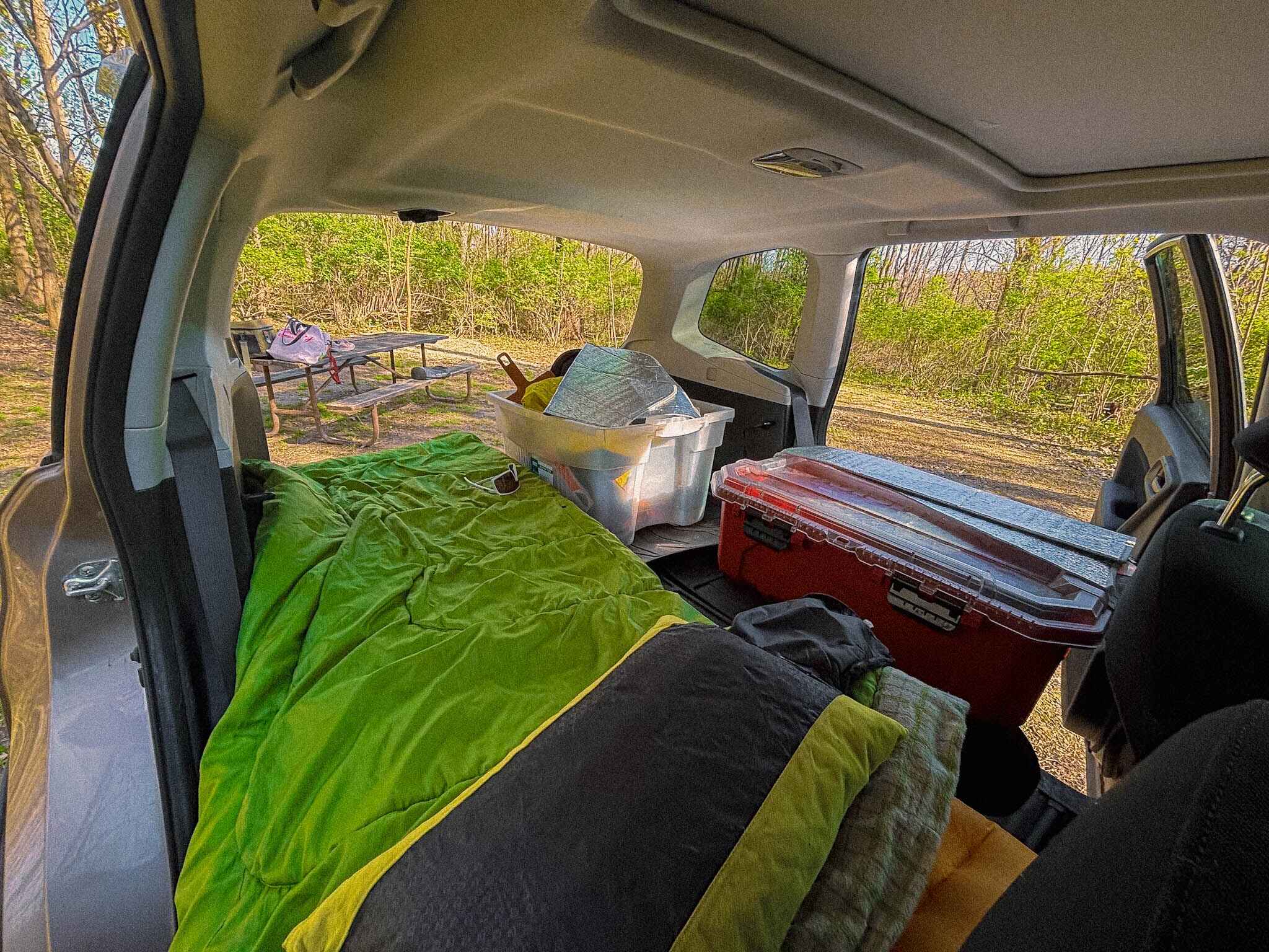 Image of a subaru budget car camping set up with a cheap coleman sleeping bag laying across the left hand side of the car