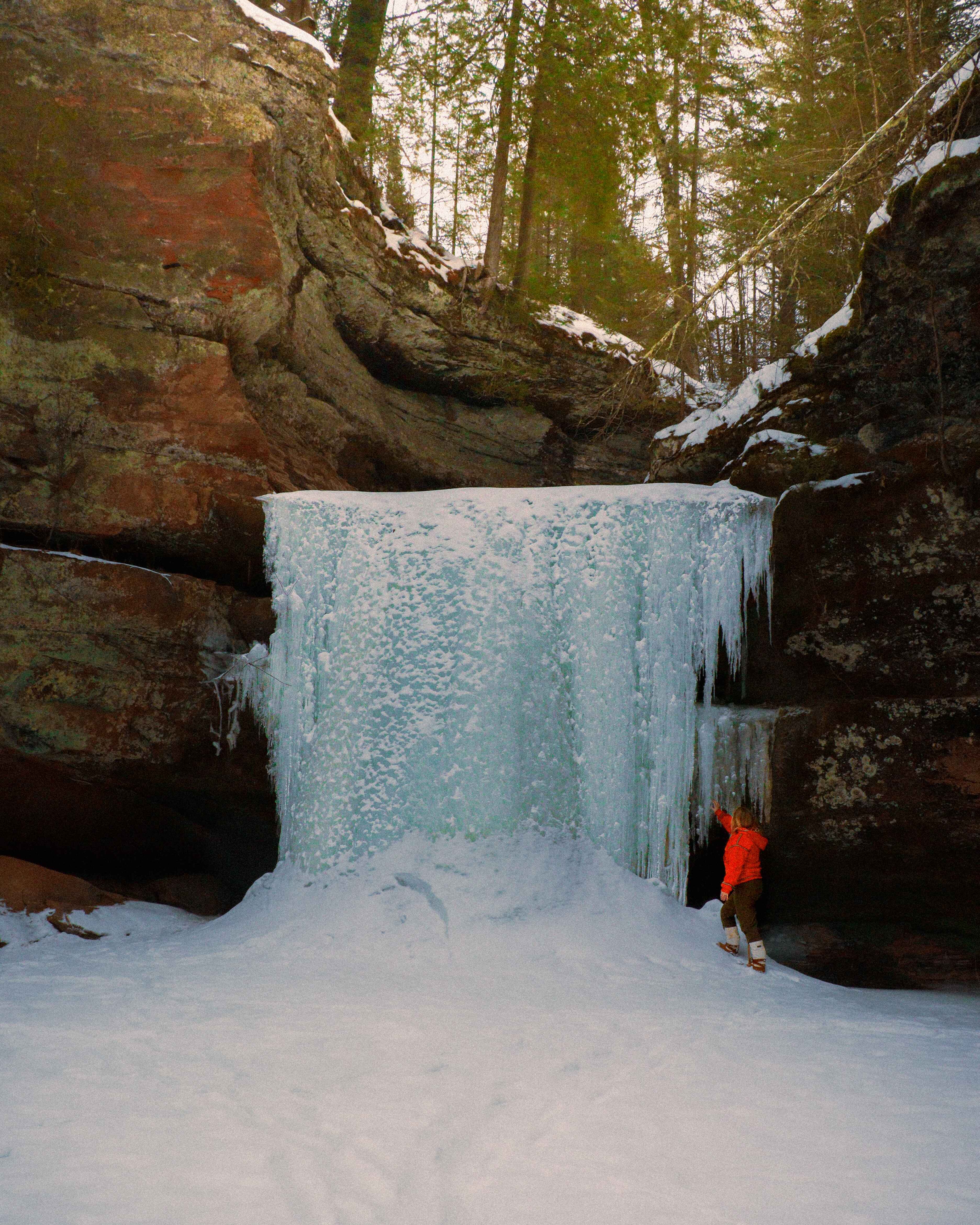 A hiker touches a frozen waterfall