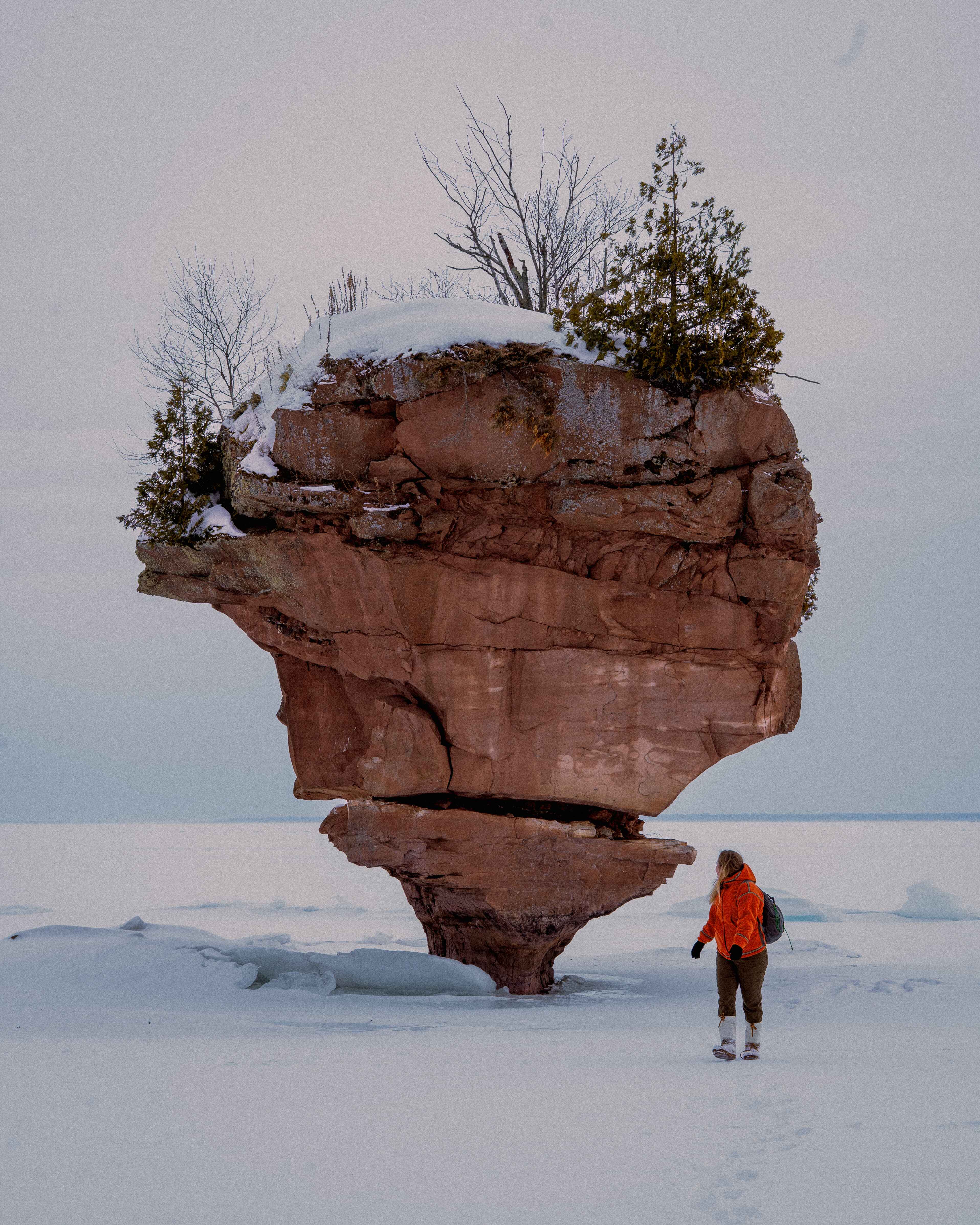 a hiker stands on frozen lake superior in bayfield wisconsin next to a frozen sea stack