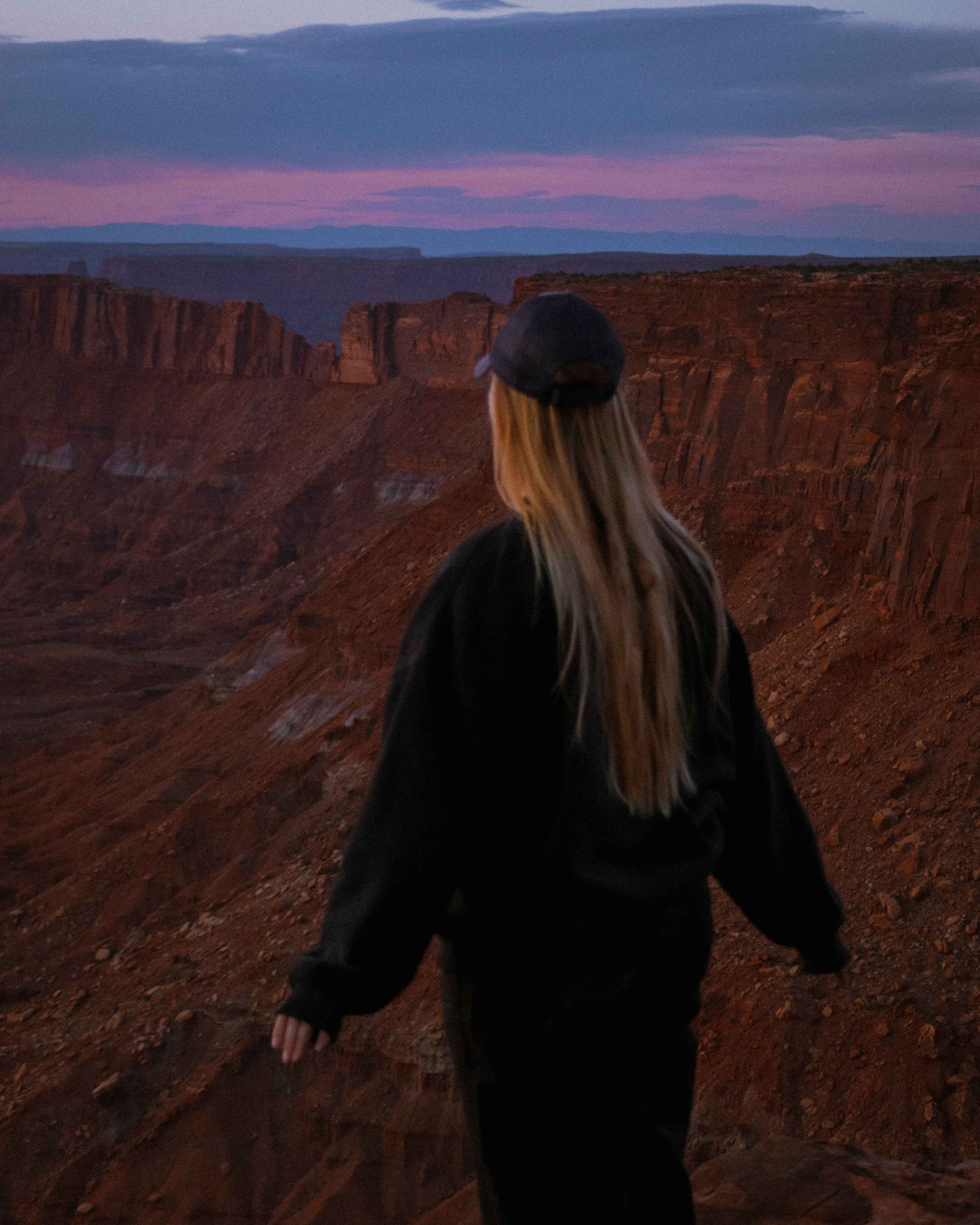 a hiker stands in front of an overlook at sunset in the desert of canyonlands national park, utah