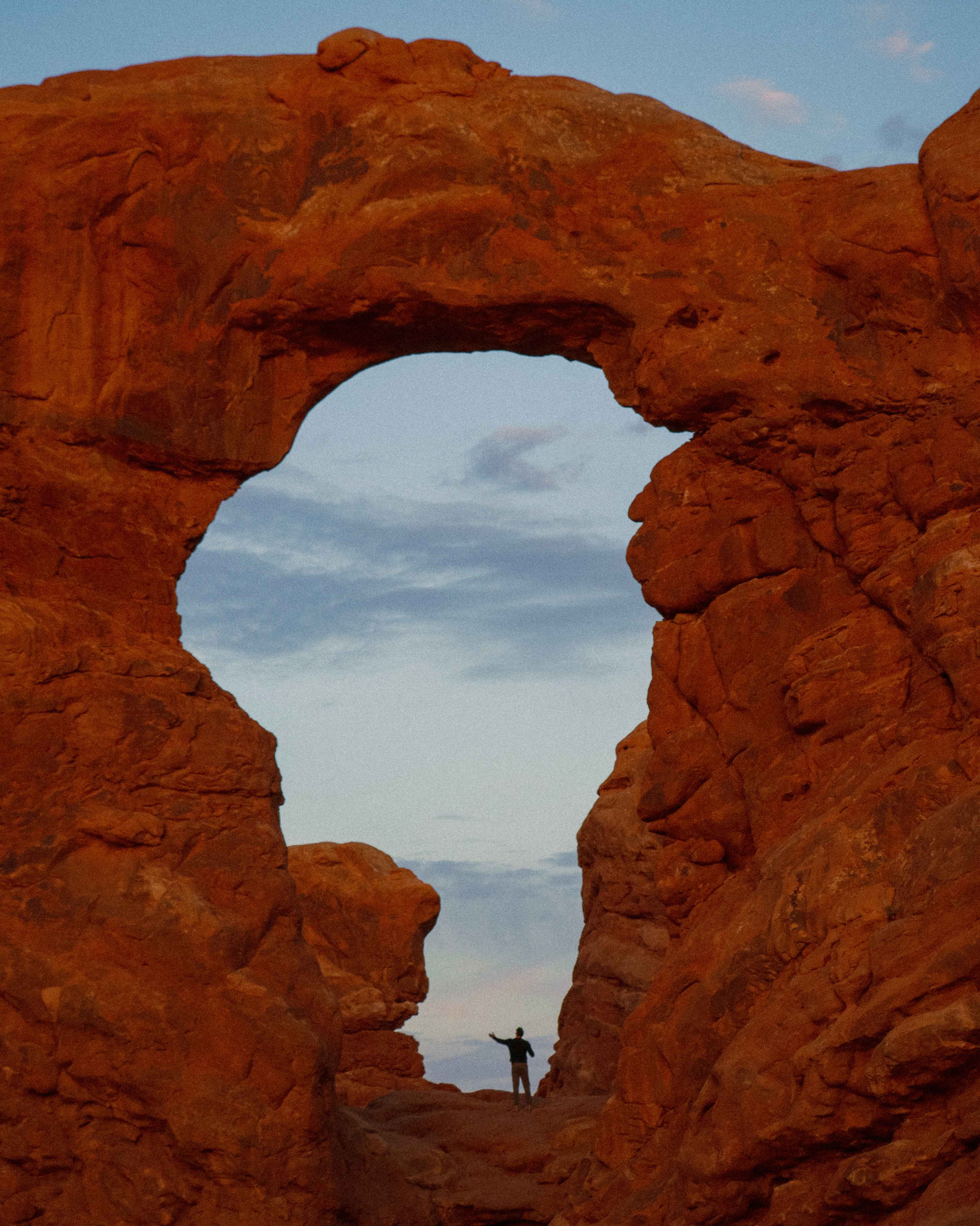 A hiker stands in an arch in Moab Arches National Park at sunrise