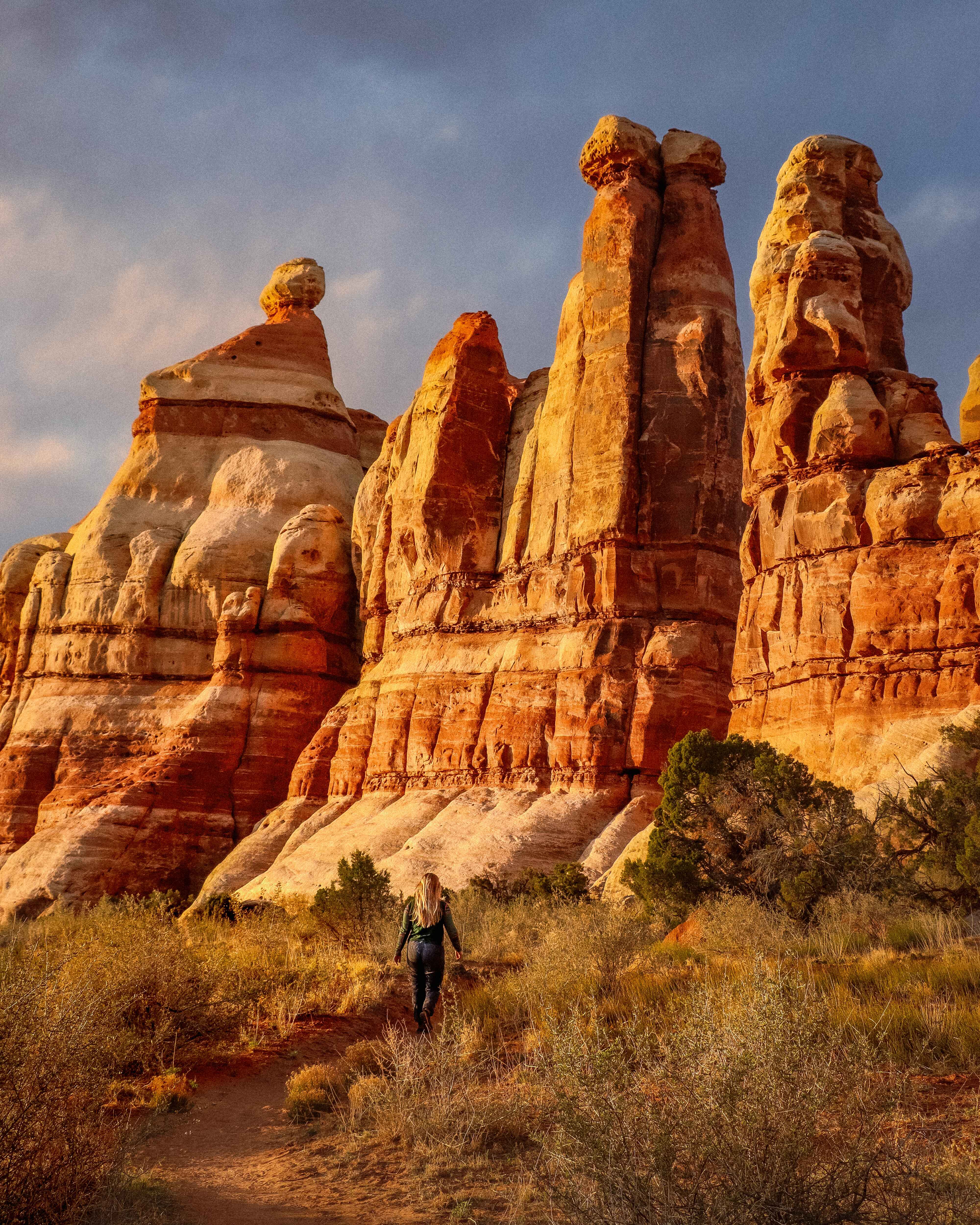 a hiker in the needles district of canyonlands national park with the hoodos backlit in the sunset