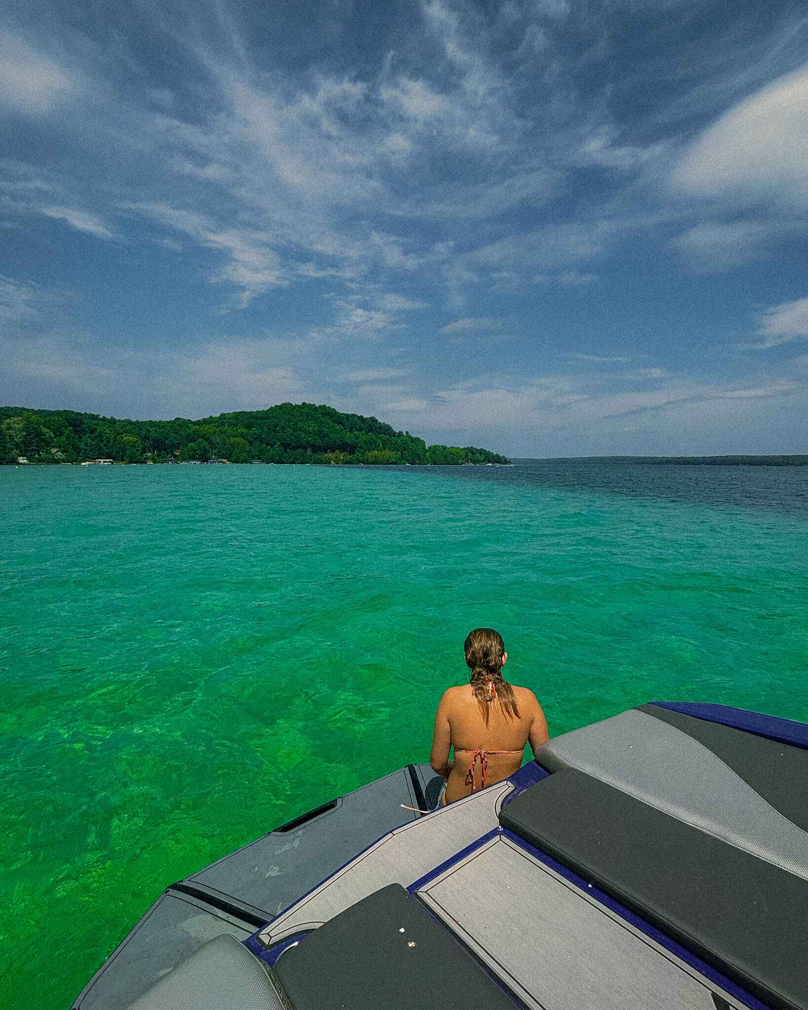 A woman swims off the back of a boat on Torch Lake, Michigan. In the image you can clearly see the dark blue drop off contrasting with the turquoise water that earned Torch Lake the moniker "Carribean of the North"