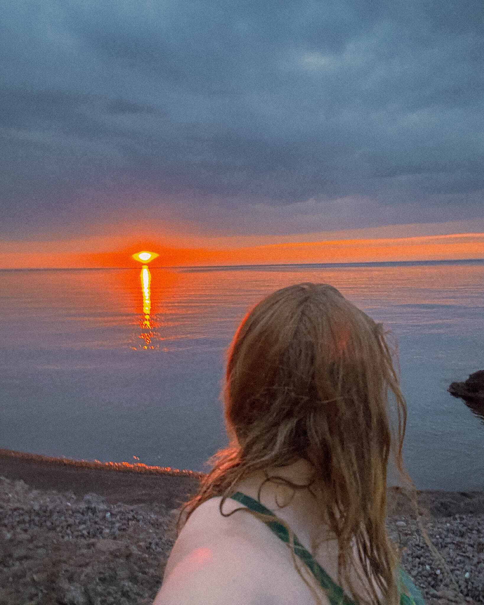 Image of a woman at the edge of lake superior as the sunsets over the lake