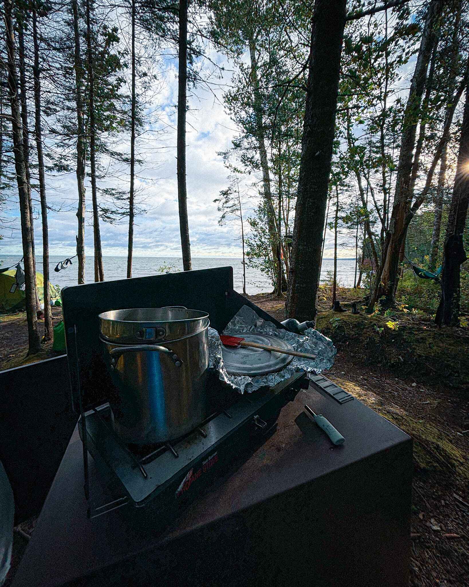 Image of big pot on a Coleman camping stove overlooking trees and a large lake in the background