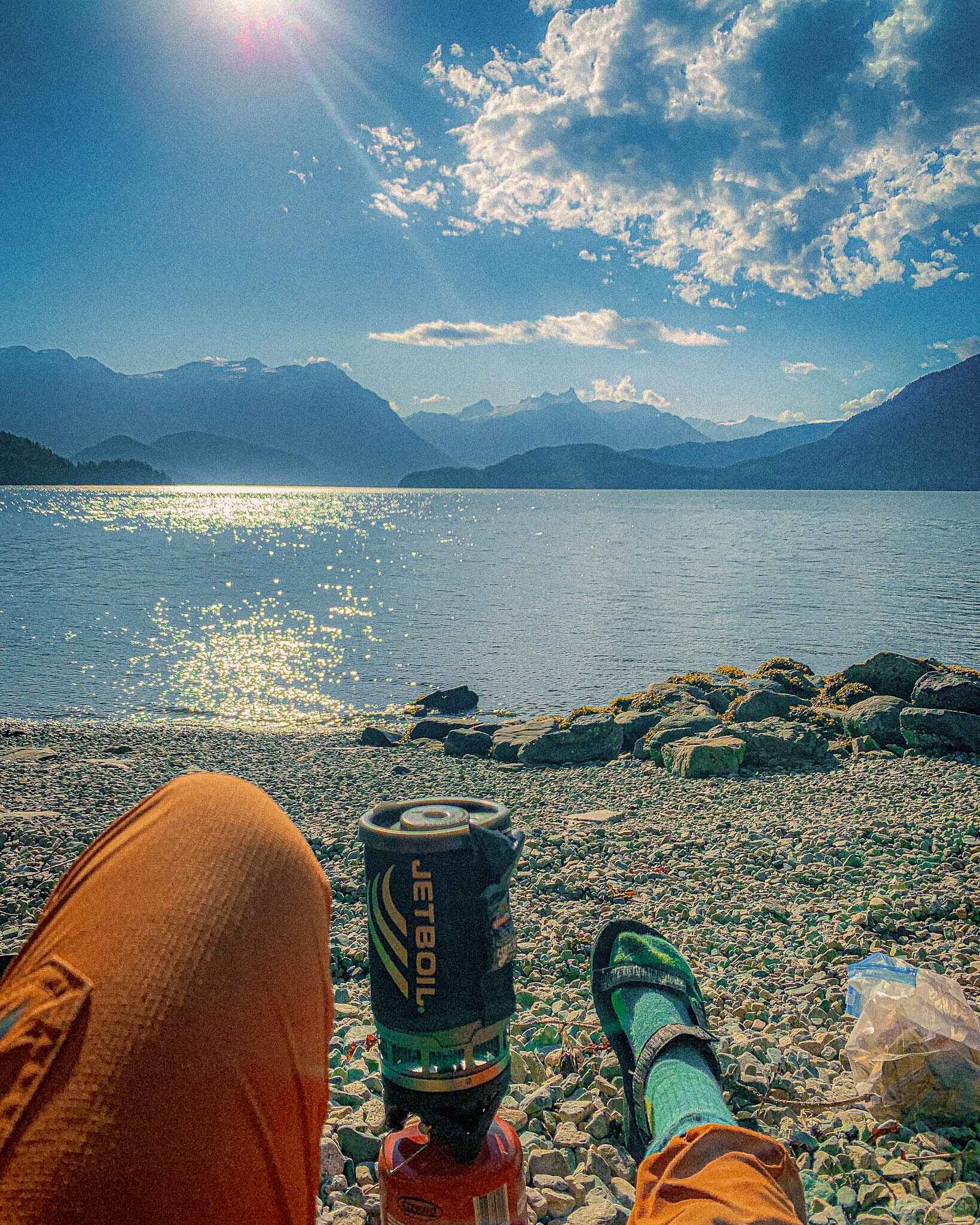 Image of a Jetboil Flash camp stove and someone's feet on a beach with mountains in the distance