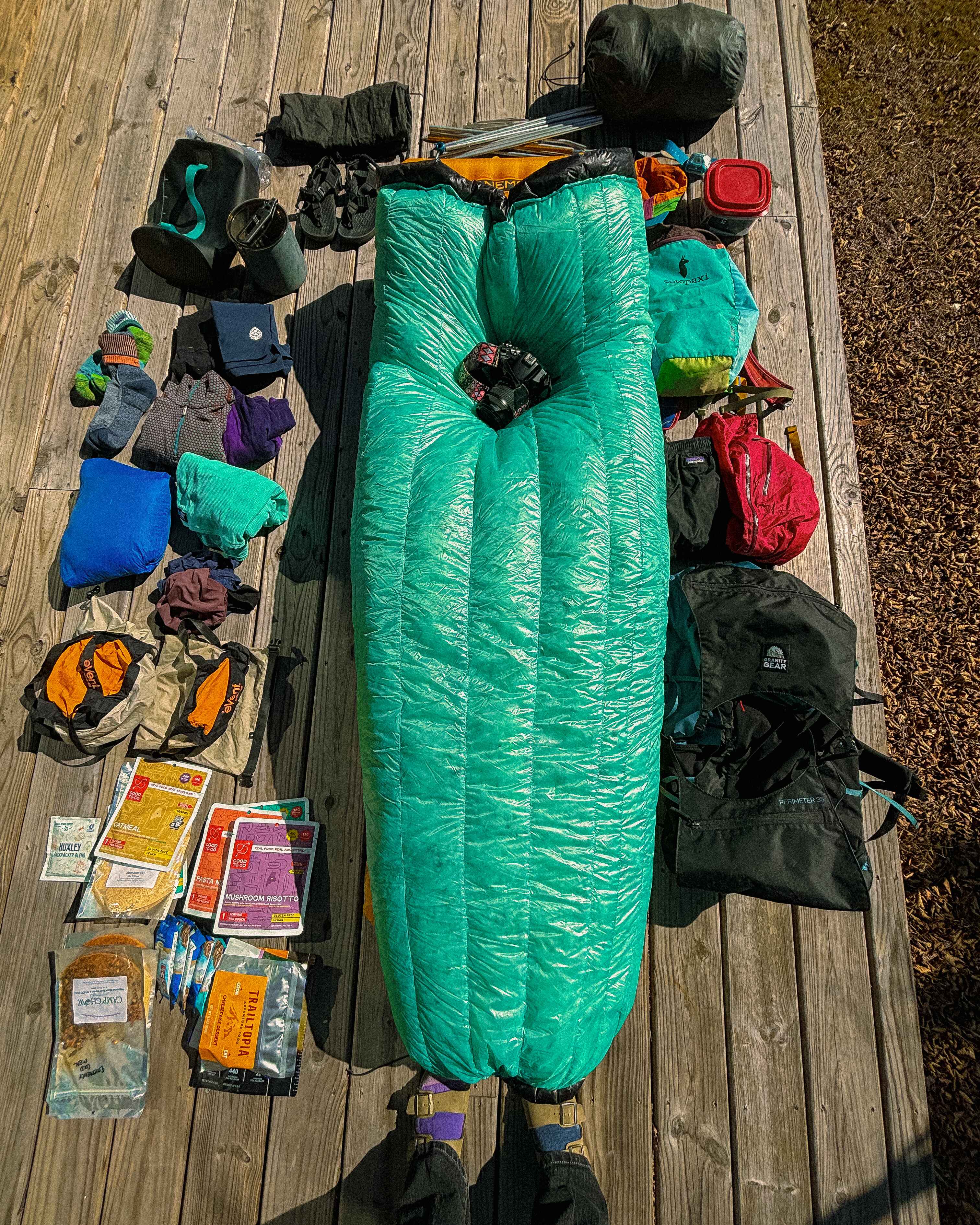 a sleeping quilt sits in the middle of a flat lay of backpacking gear