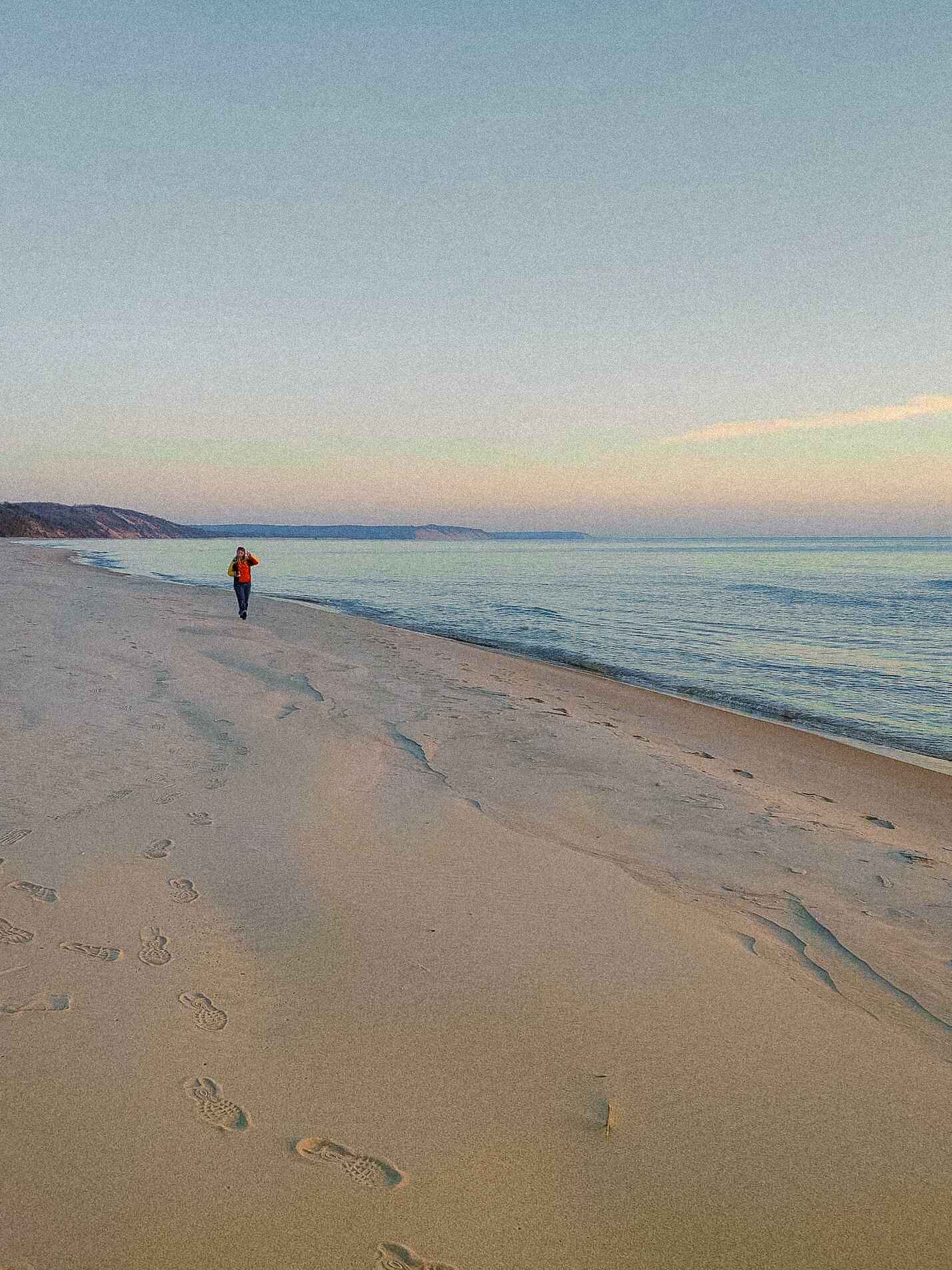 A small hiker walks on the edge of Lake Michigan in the sand around sunset 