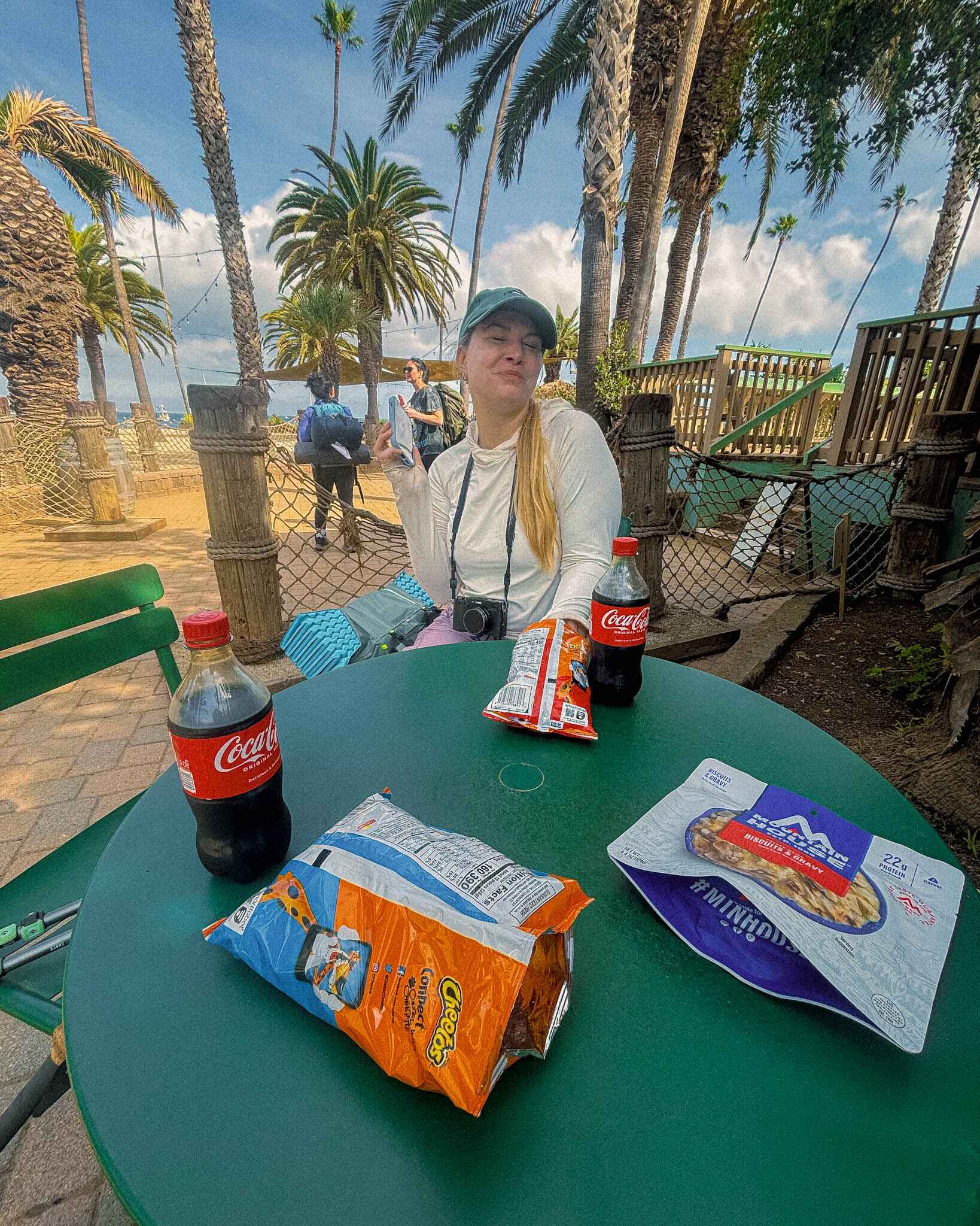a hiker stops to refuel on the transcatalina trail with junk food, palm trees in the background