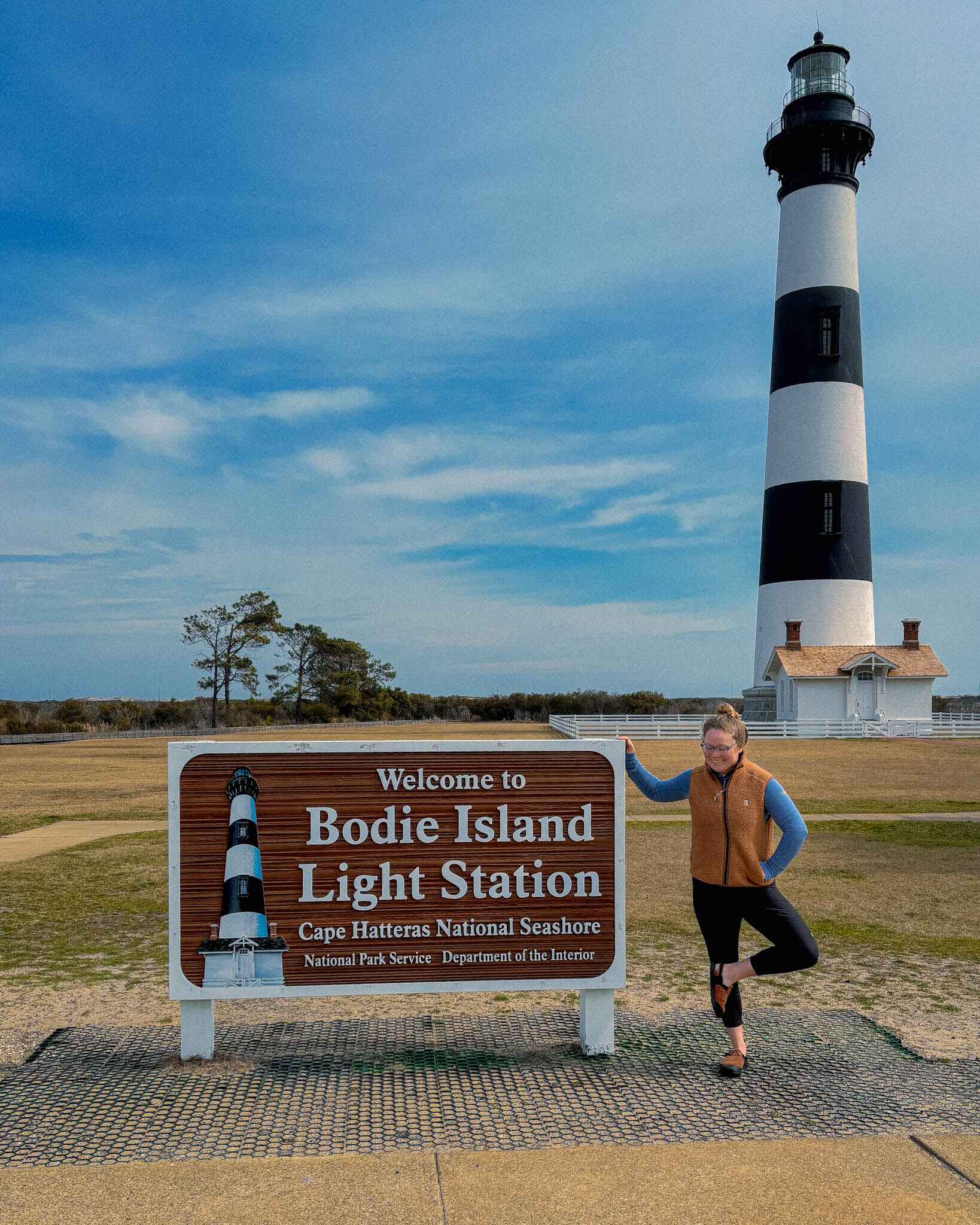 A hiker stands next to the Bodie Island Light Station Sign in Cape Hatteras National Seashore