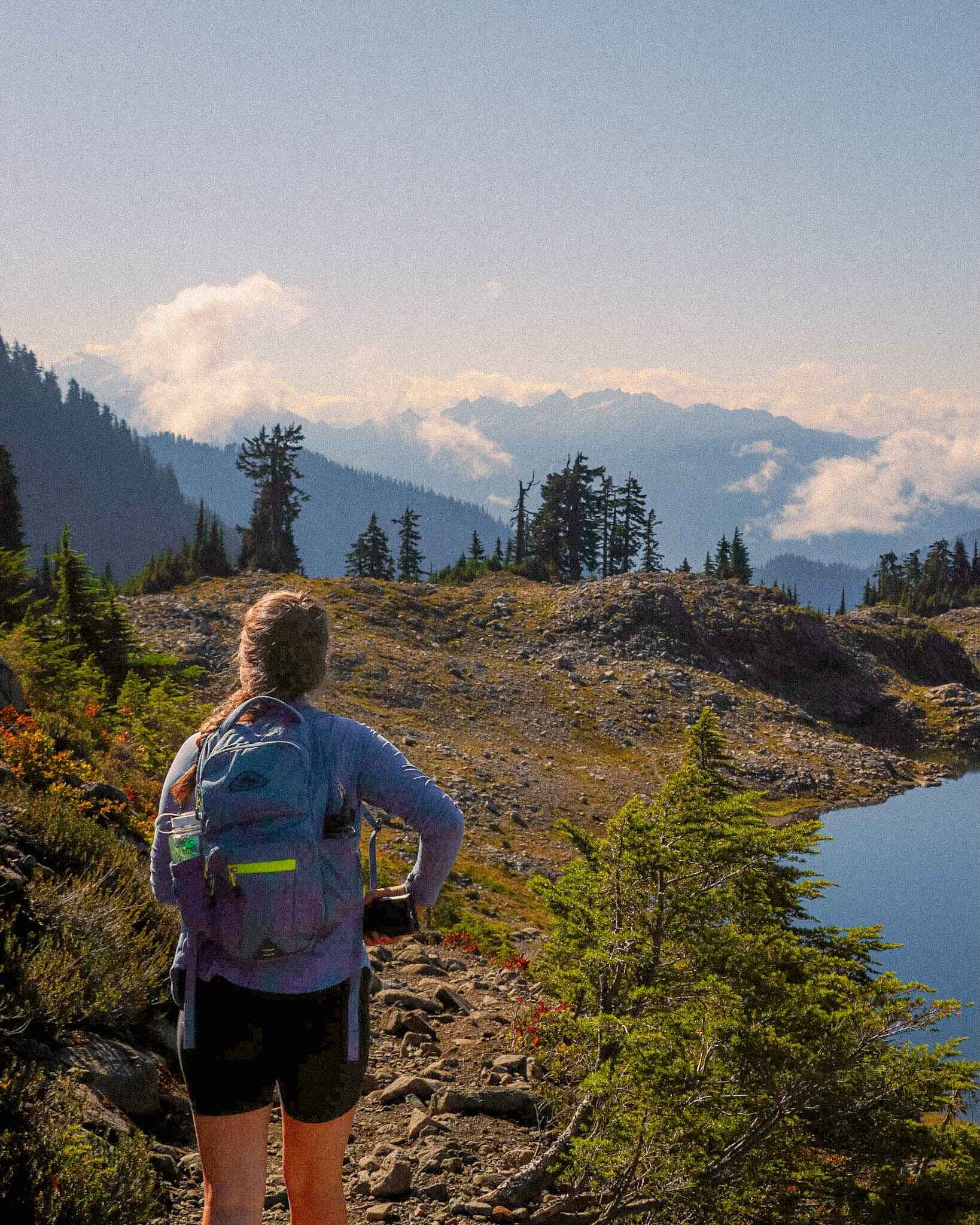 a hiker with a backpack by an alpine lake in legging style hiking shorts