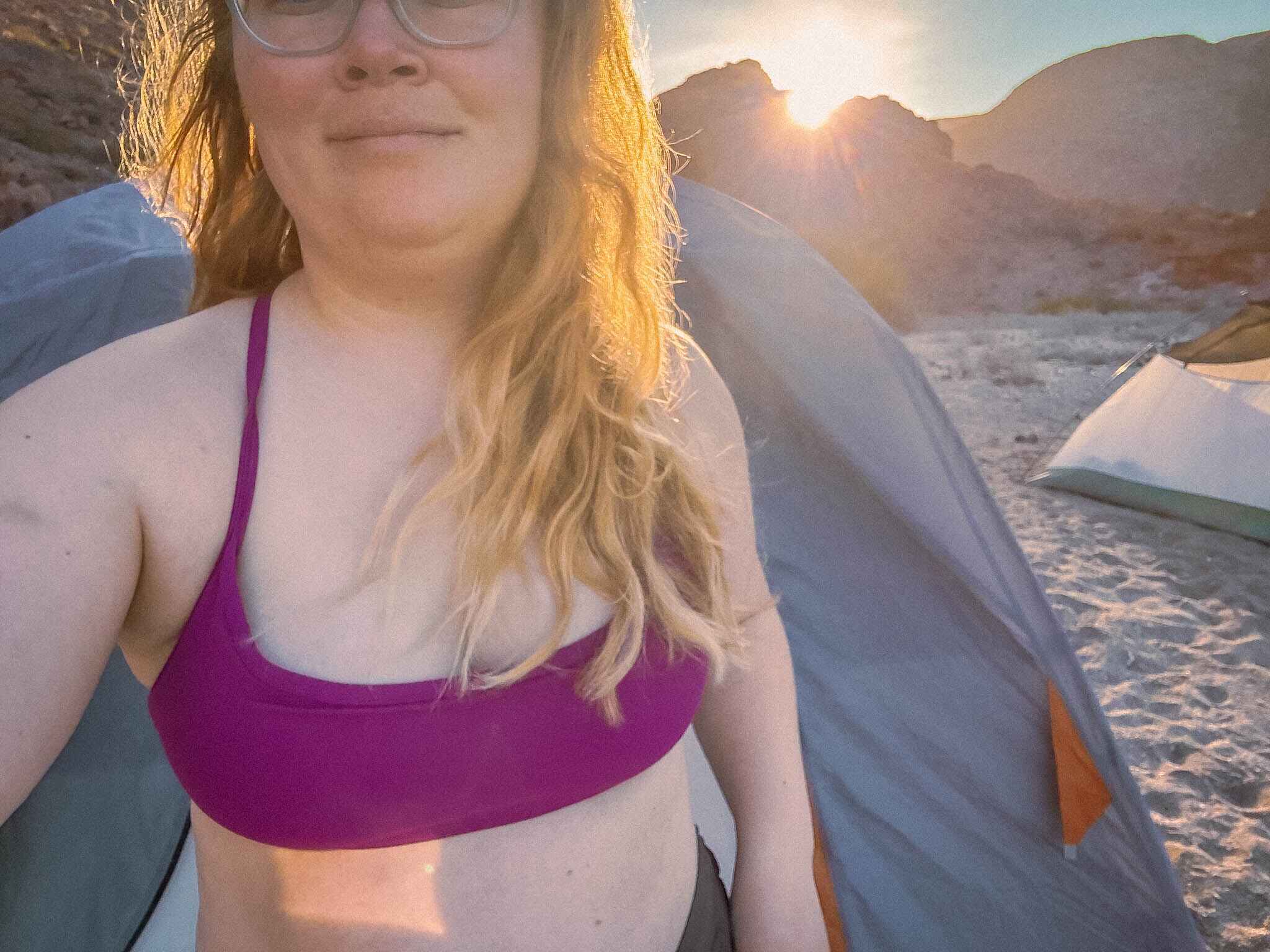 image of a woman standing in front of a tent wearing a purple sports bra while camping in the desert on an island in baja