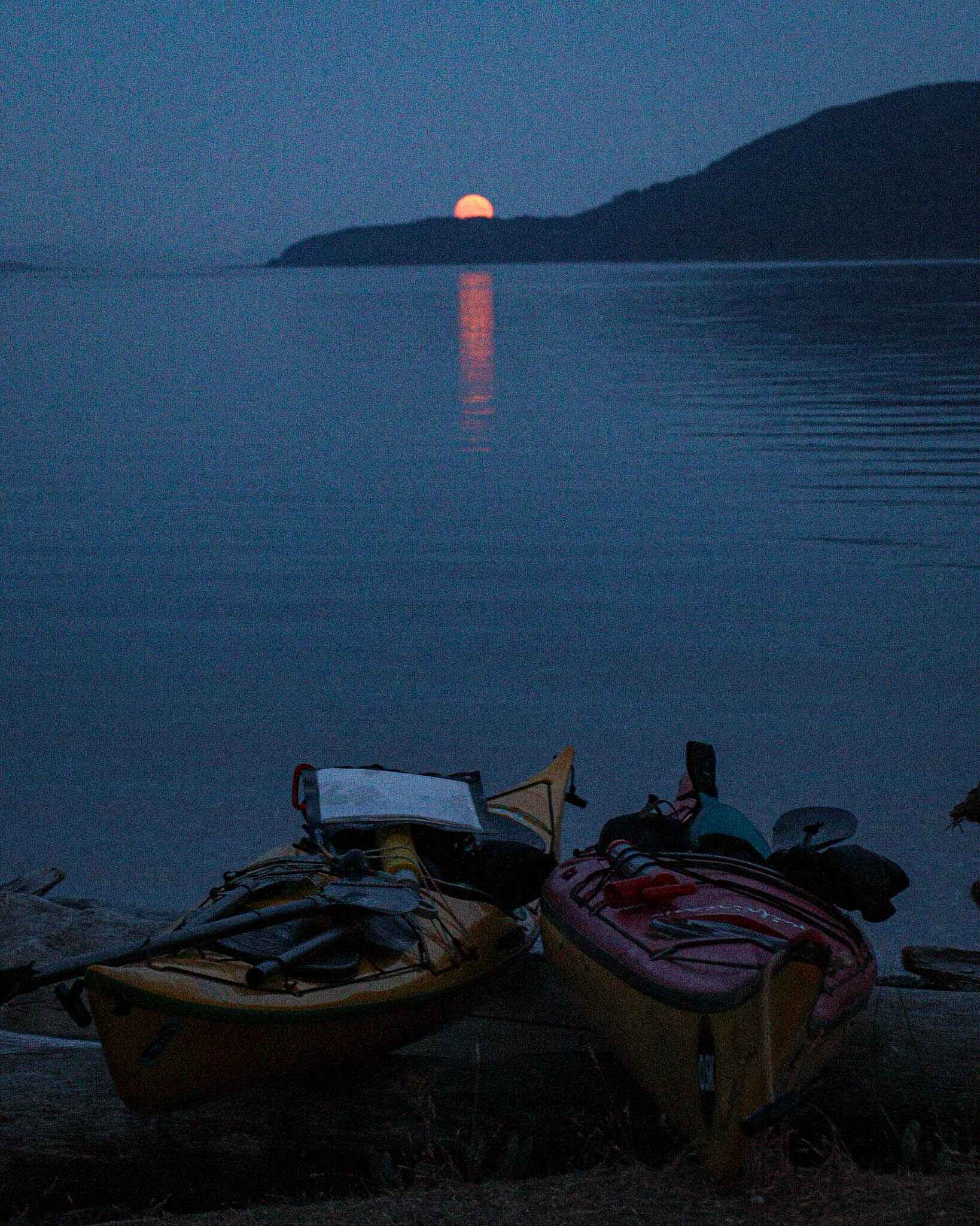 a full moon rises over the ocean wiht kayaks in front of the water