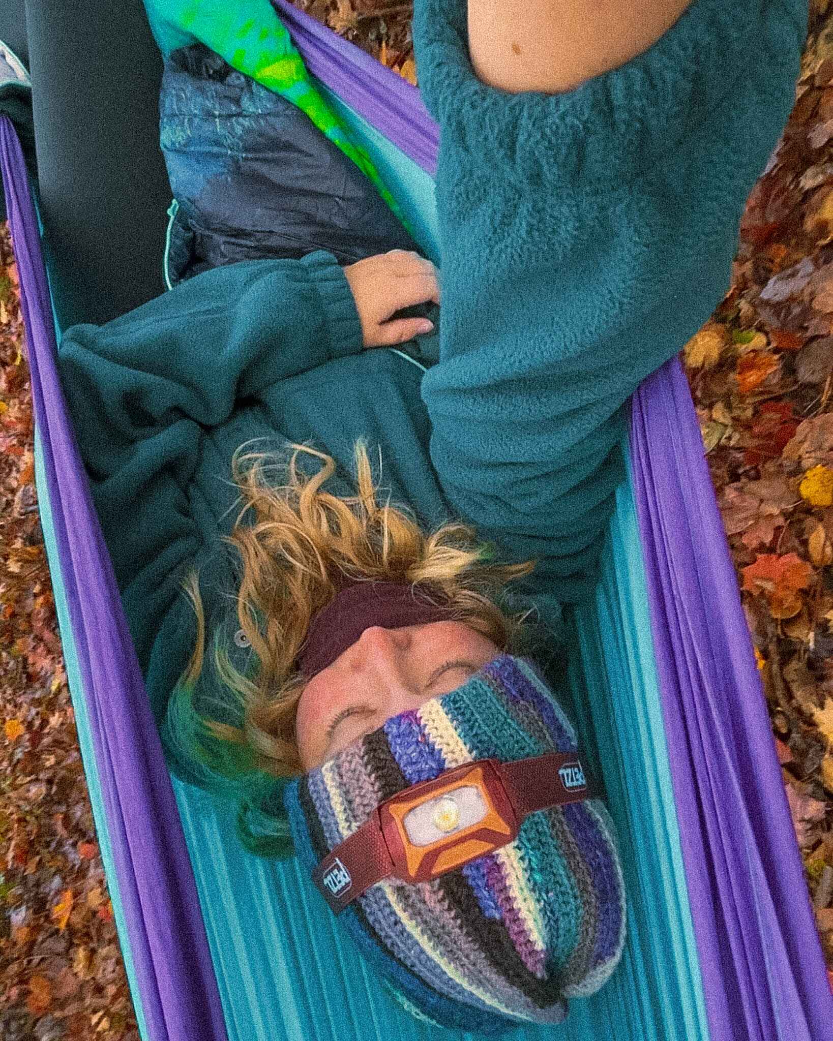 a hiker sits in a hammock with a headlamp on