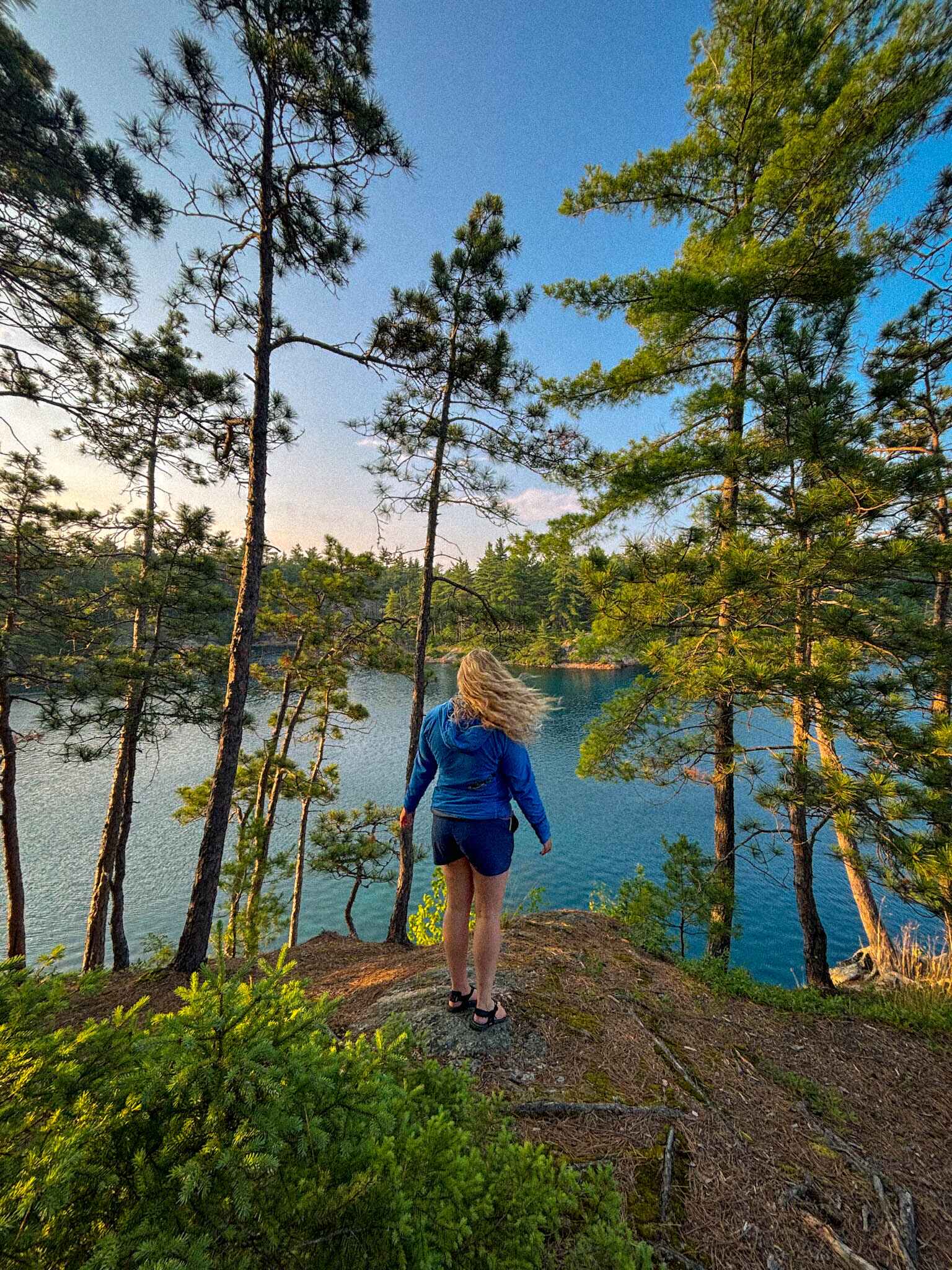 a hiker stands over a blue lake in Killarney Provicial park