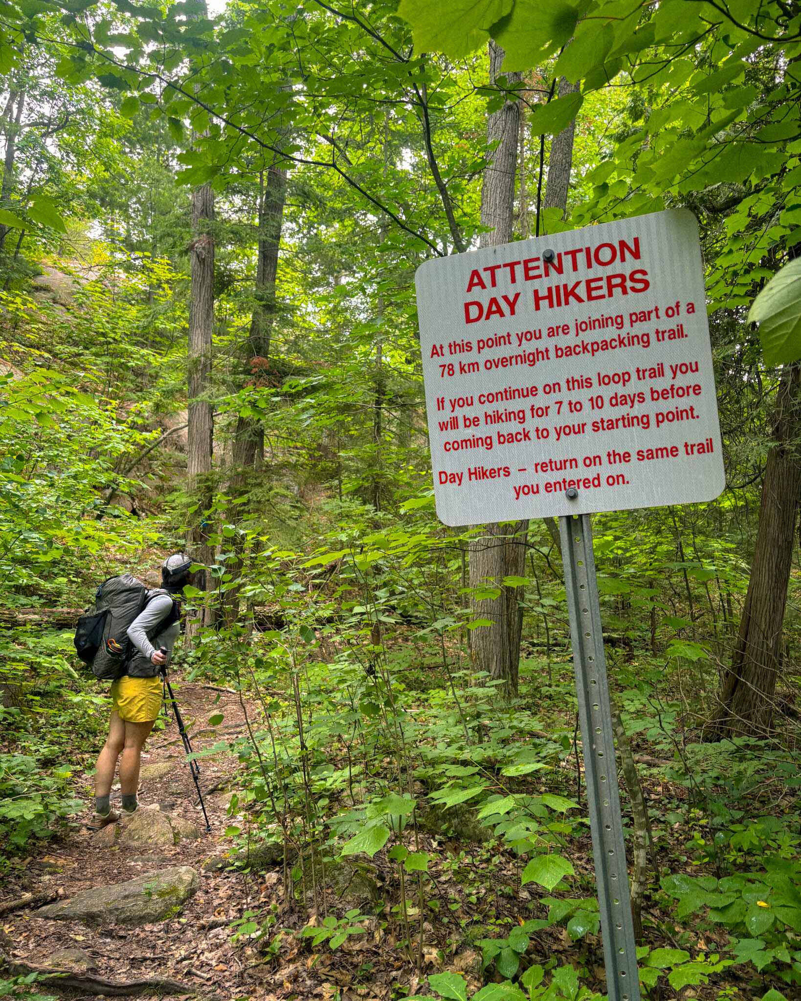 backpacker stands next to a warning sign on the La Cloche Silhouette Trail