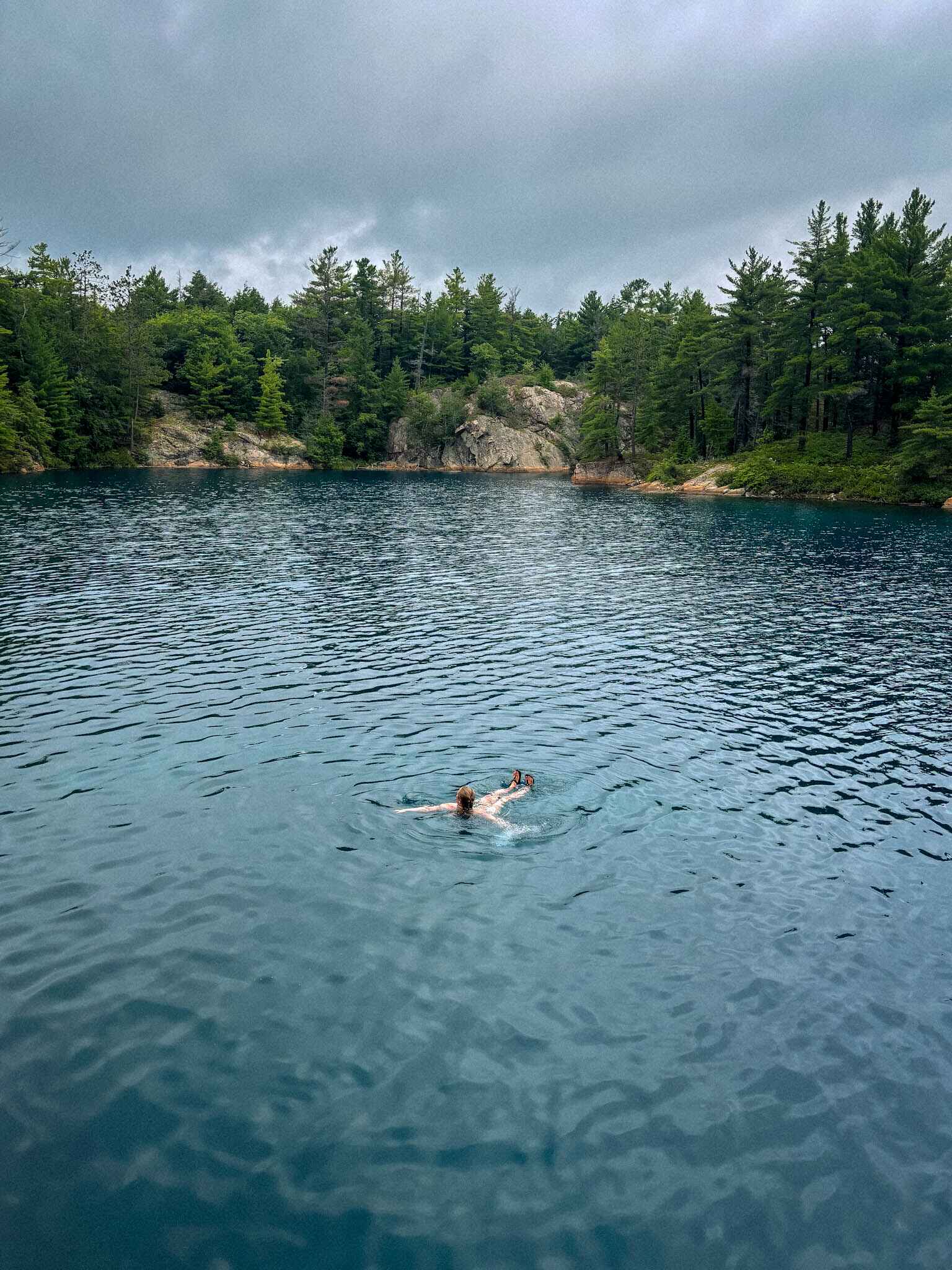 a hiker swims in a blue lake on the La Cloche Silhouette Trail