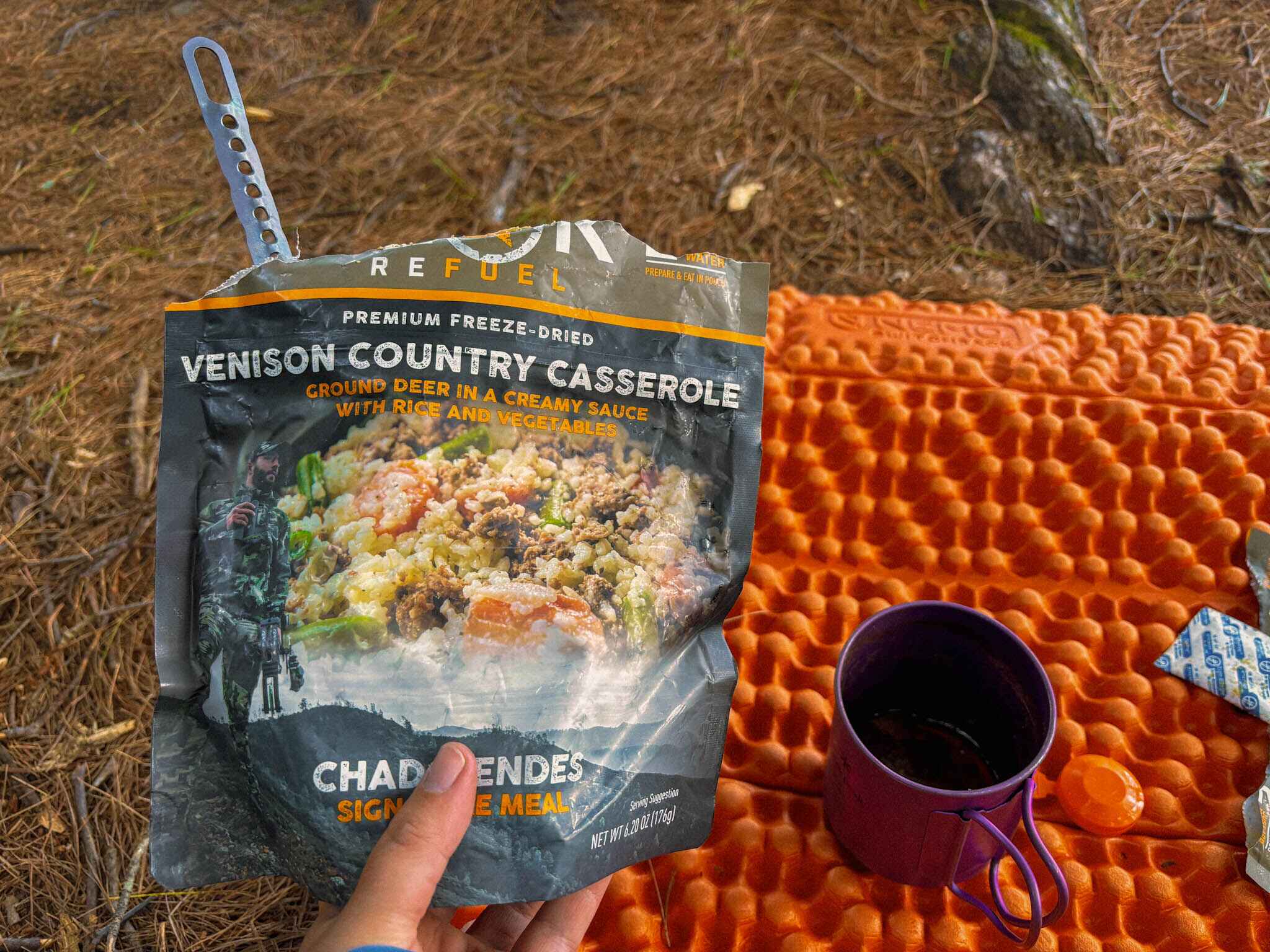 image of peak refuels venison country casserole held to camera with a sleeping pad and coffee mug also in frame