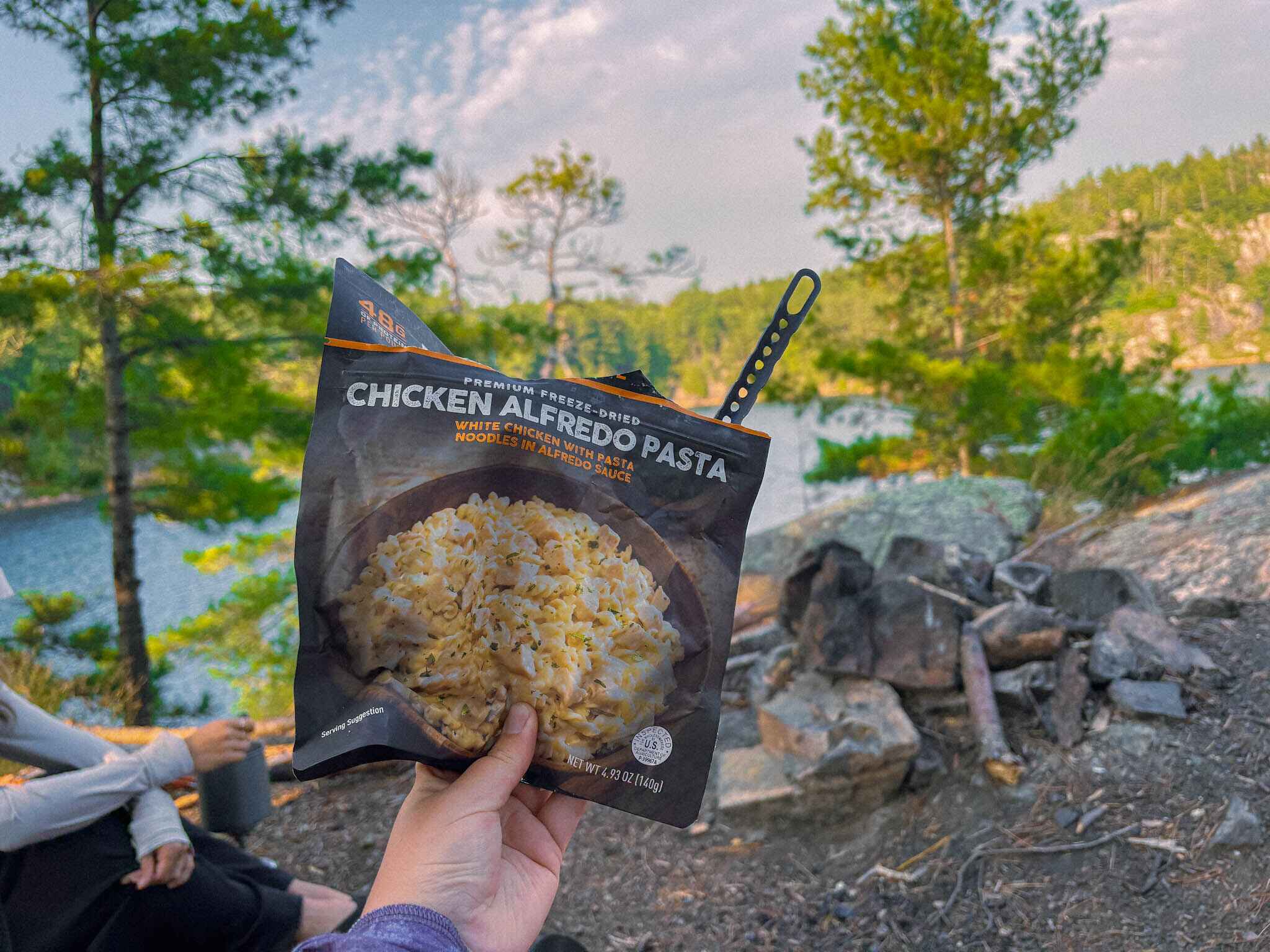 Chicken alfredo pasta backpacking meal held to camera at a campsite. in Canada
