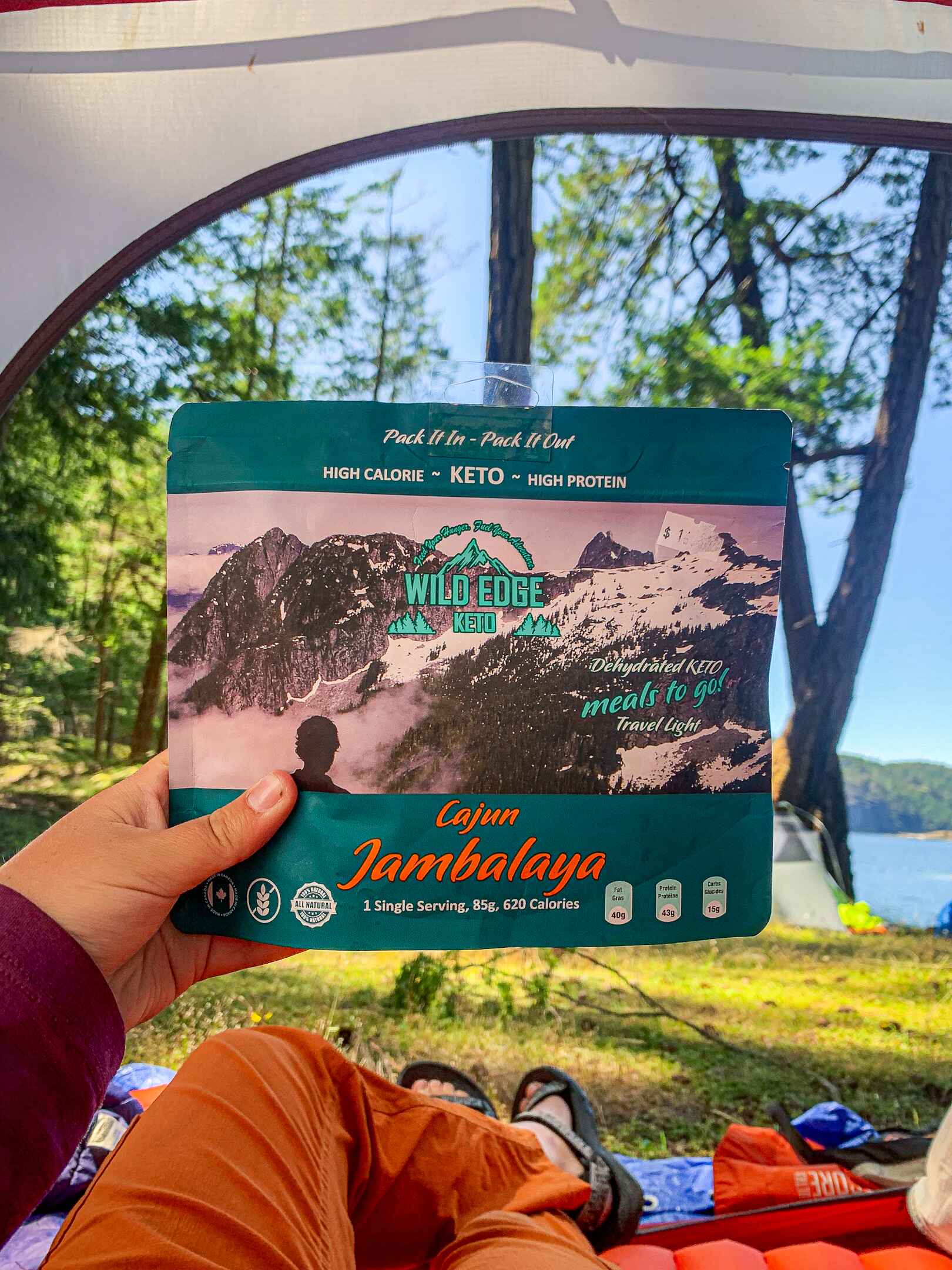 a backpacking meal is held up to the camera while a hiker lounges in a tent
