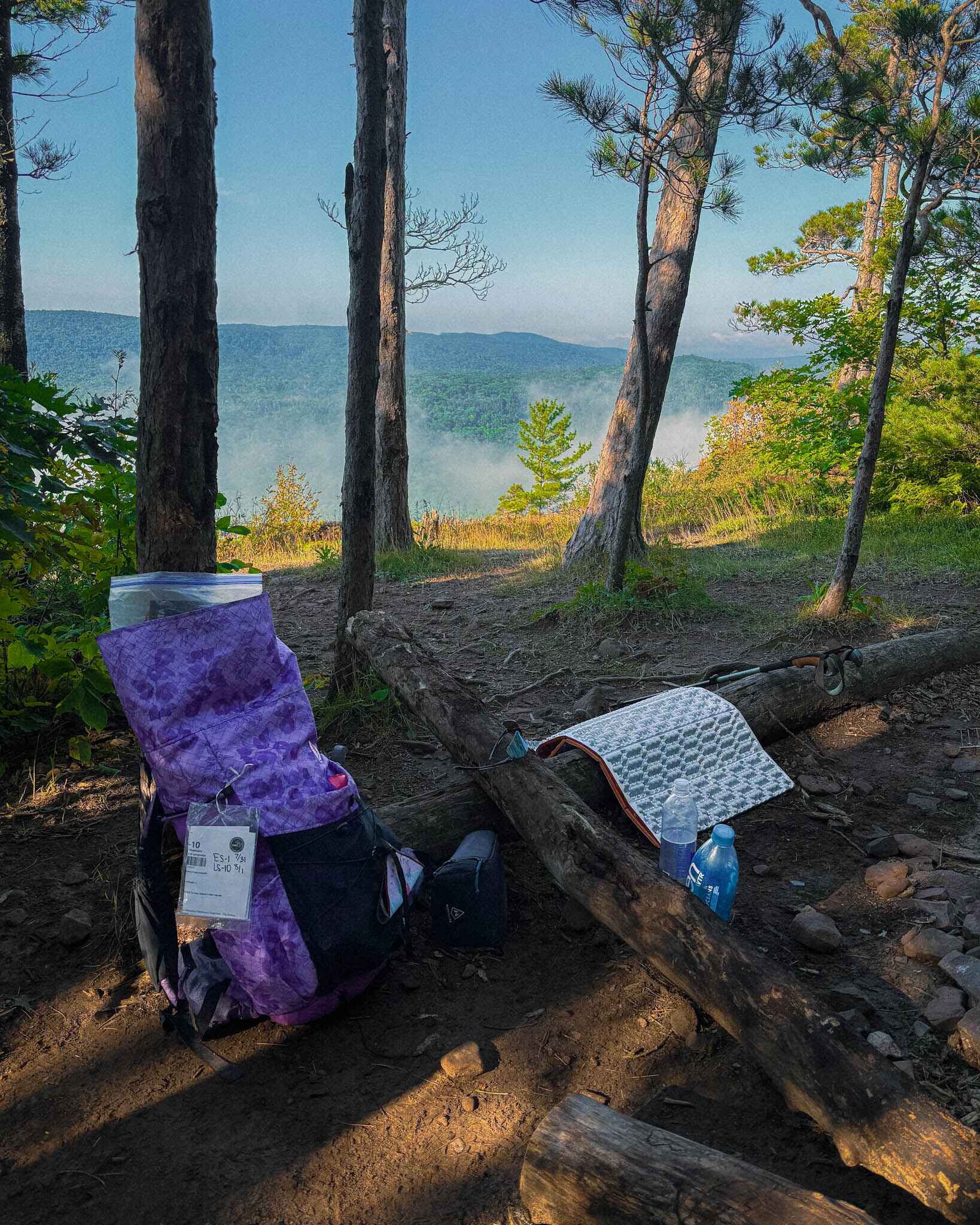 image of a budget sleeping pad on the ground next to a backapcking bag in the forest at the edge of a ridge with fog in the valley below