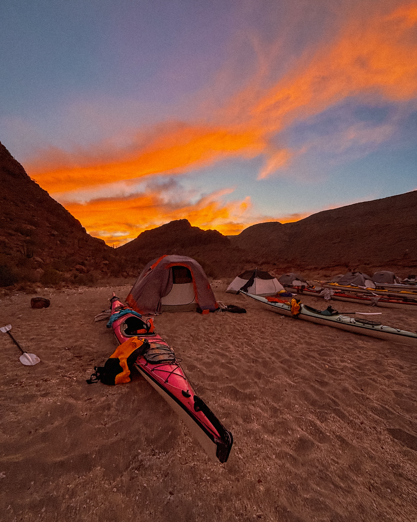 image of a kayak on a beach with a Kelty brand budget tent behind it as the sun rises in a canyon in the background