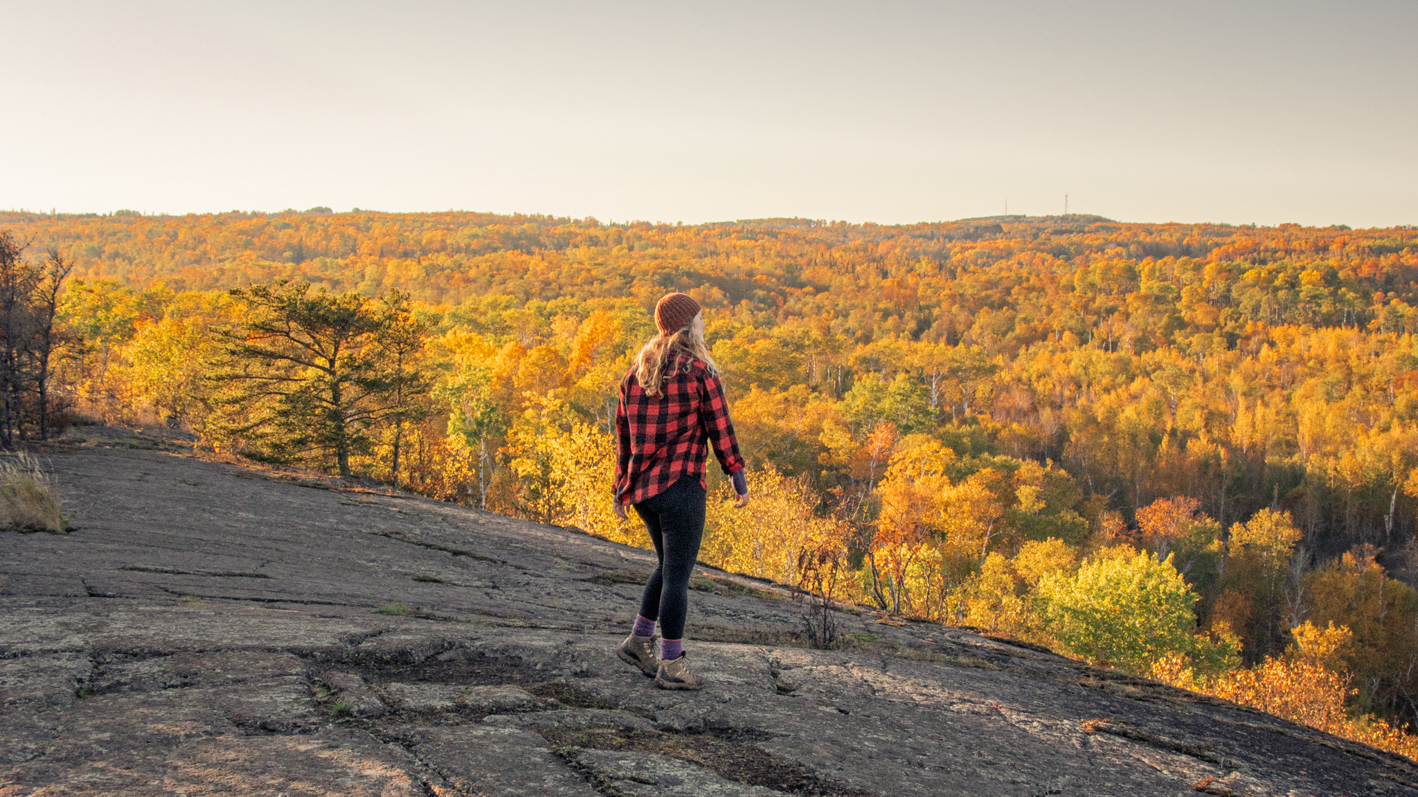 a hiker stands on a bald overlooking a sea of fall color in Northern Minnesota