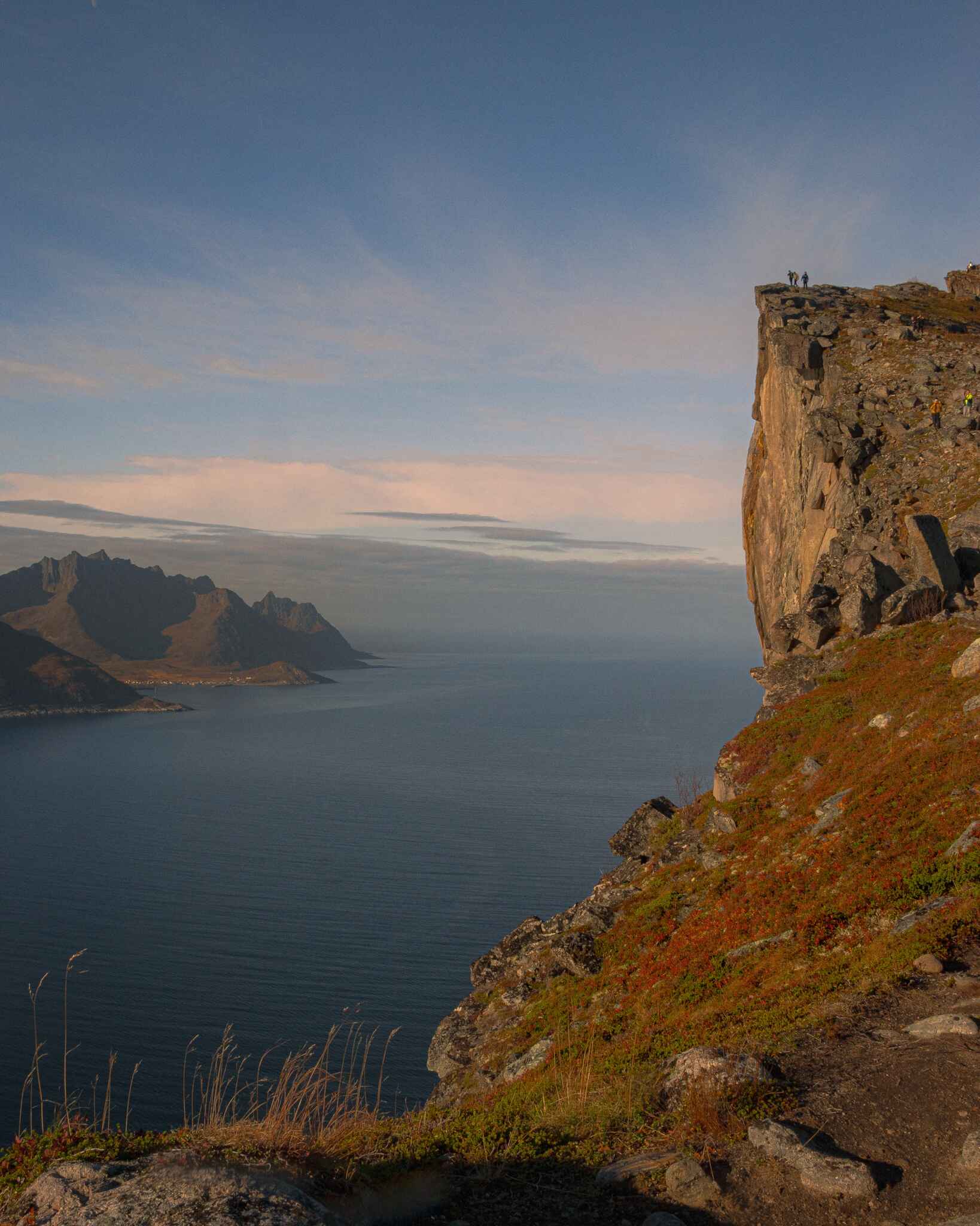 image of small hikers standing above a cliff at the edge of the ocean