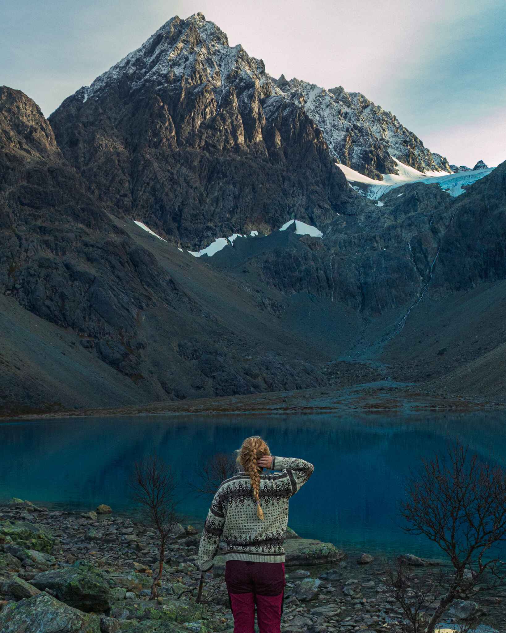 Image of me (the author, Maddy) standing in front of a blue glacial fed lake in the Lyngen Alps, two hours north of Tromso