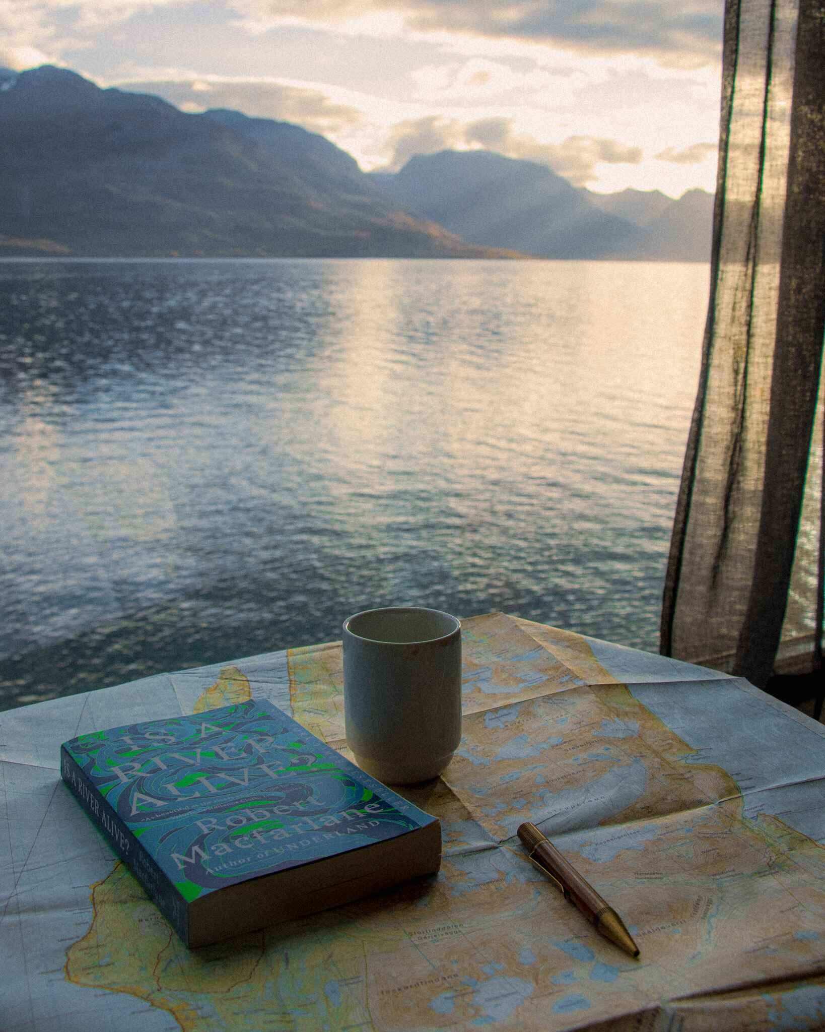 image of a book and coffee cup in front of a window looking out over the fjord at the Aurora Distillery Cabins in the Lyngen Alps