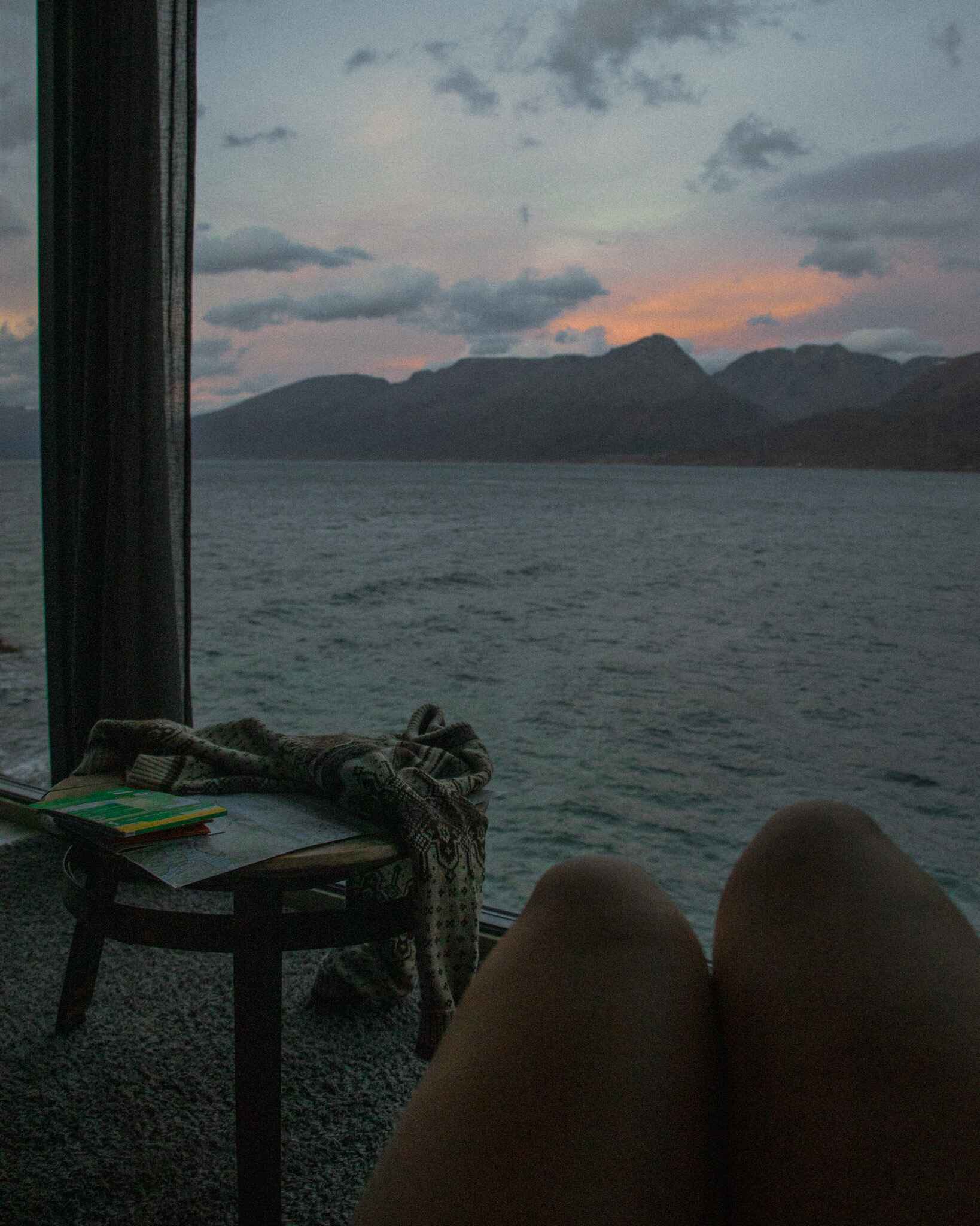 Image of a sweater and maps on a table in front of a window looking out over the fjord at the Aurora Distillery Cabins in the Lyngen Alps