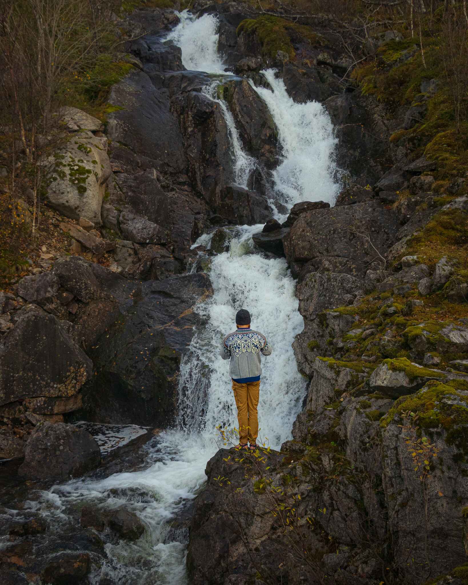 a hiker stands in front of a waterfall in senja, norway