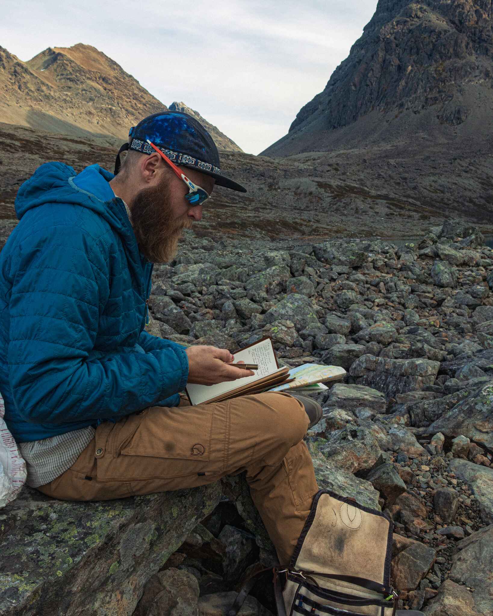 a hiker takes notes in a notebook while sitting on a rock in a boulderfield in the mountains