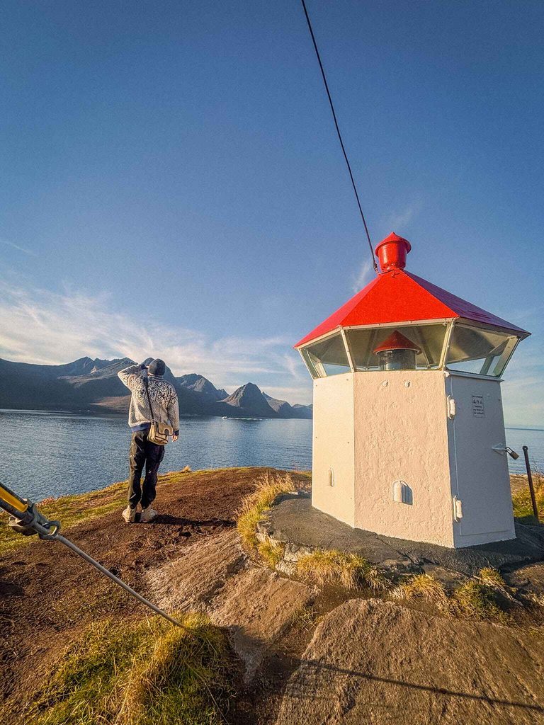 A hiker stands by a lighthouse (fyr) on Husøy, Senja Island, Norway