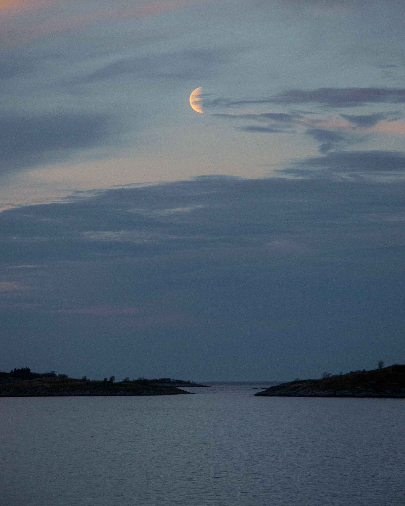image of a quarter moon rising over the ocean in Senja, Norway