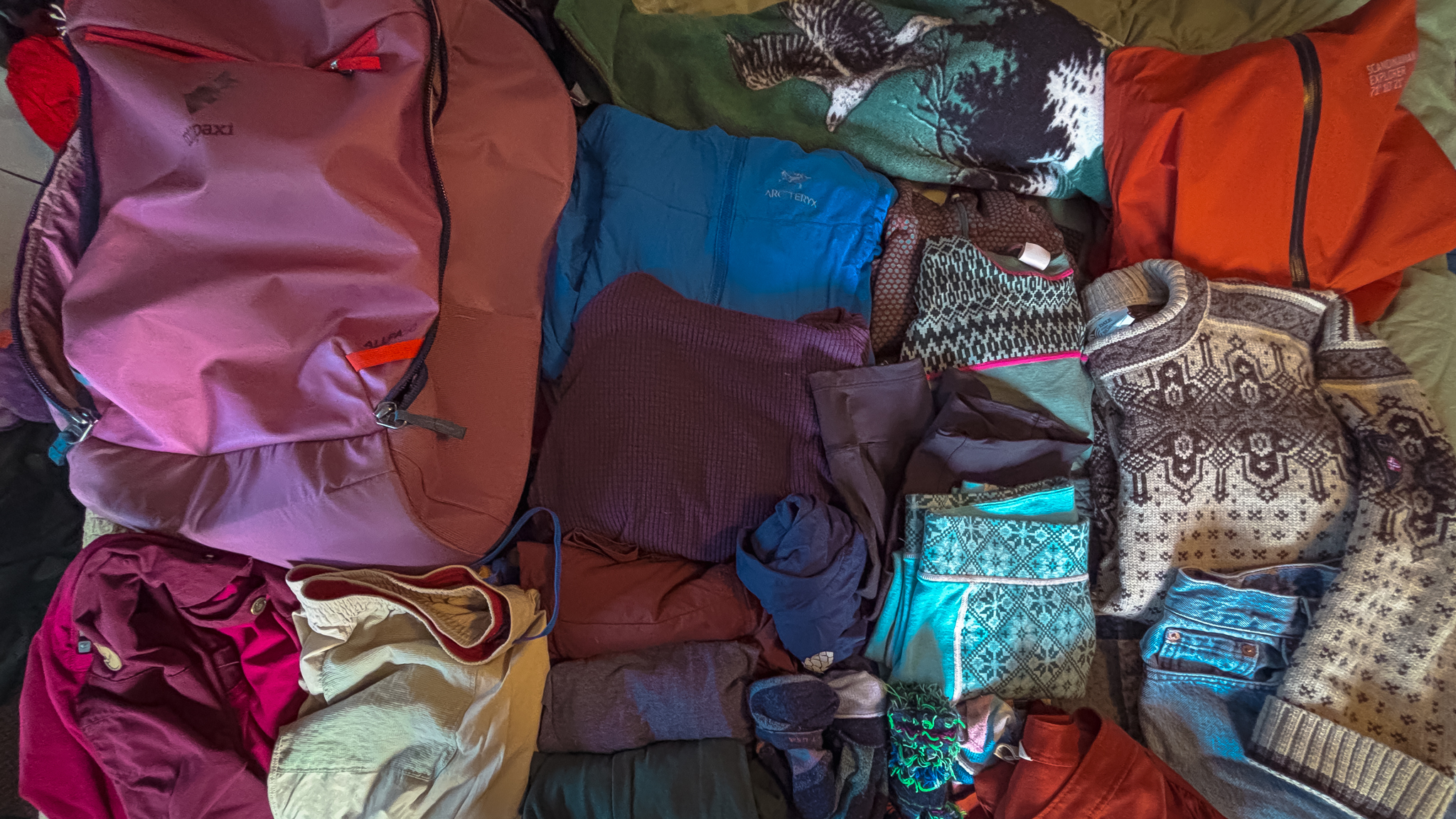 image of folded clothes next to a backpack while packing for a trip