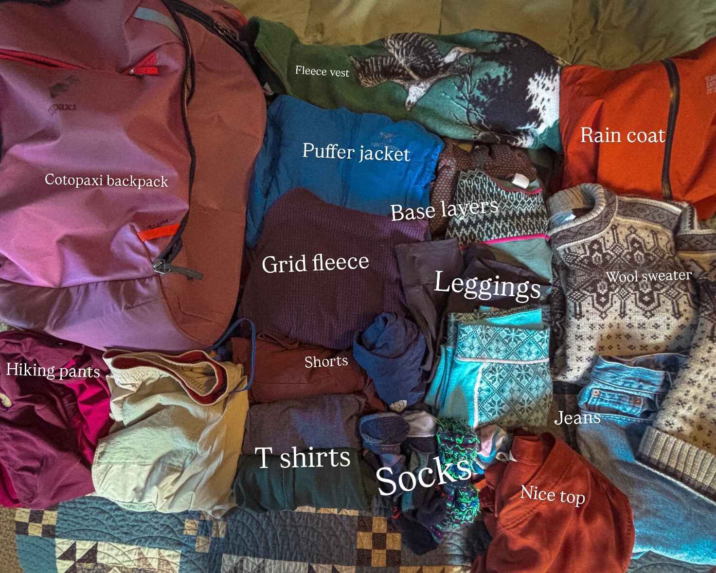 Image of a flat lay of everything I (the author, maddy) packed for Norway, labeled. Image includes Cotopaxi backpack, hiking pants, fleece vest, puffer jacket, grid fleece, shorts, t-shirts, base layers, leggings, socks, a rain coat, wool sweater jeans and a nice top.
