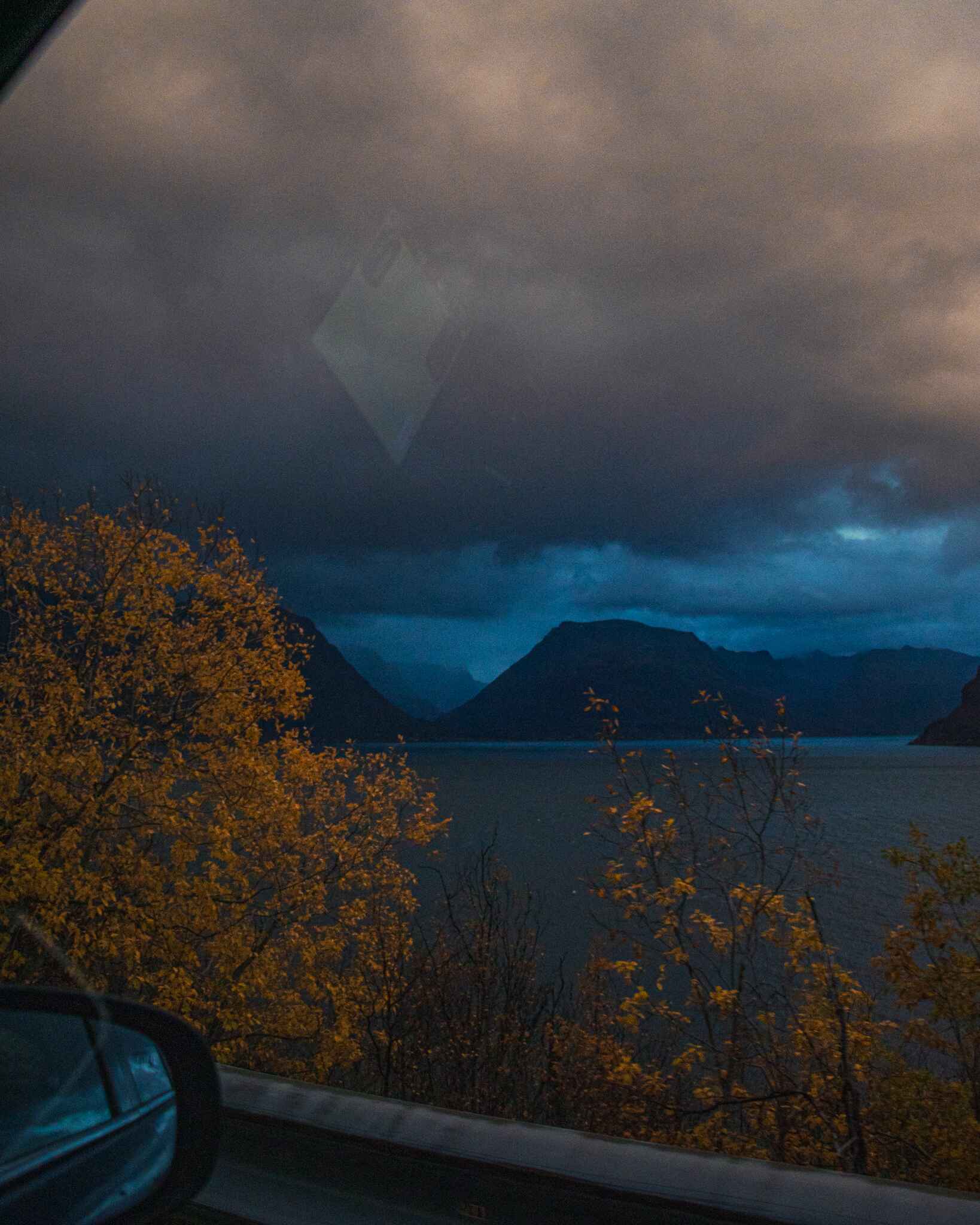 image of a moody fjord and fall color out of a car window