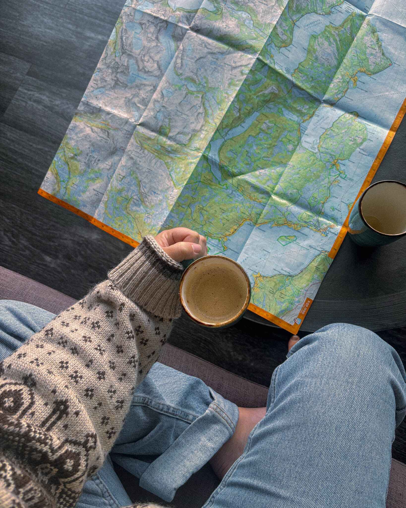 image of a woman in a wool sweater holding a cup of coffee by a map