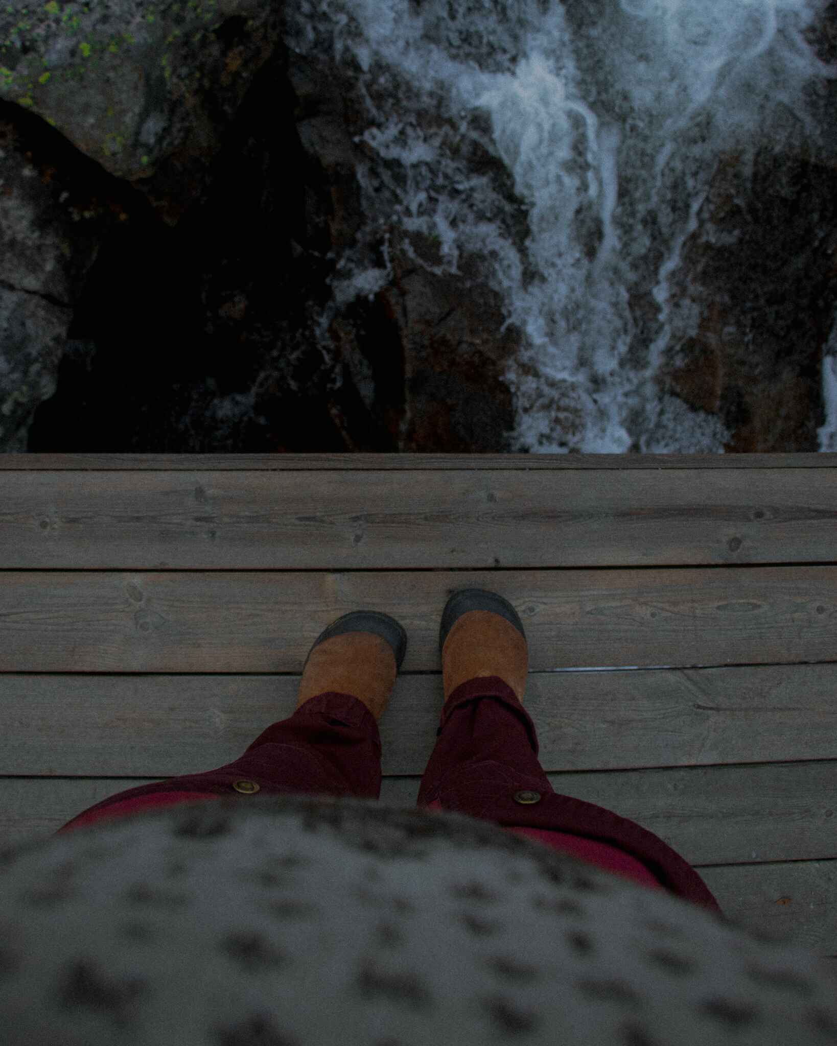 image of a hiker's legs and feet on a bridge looking down at a small waterfall
