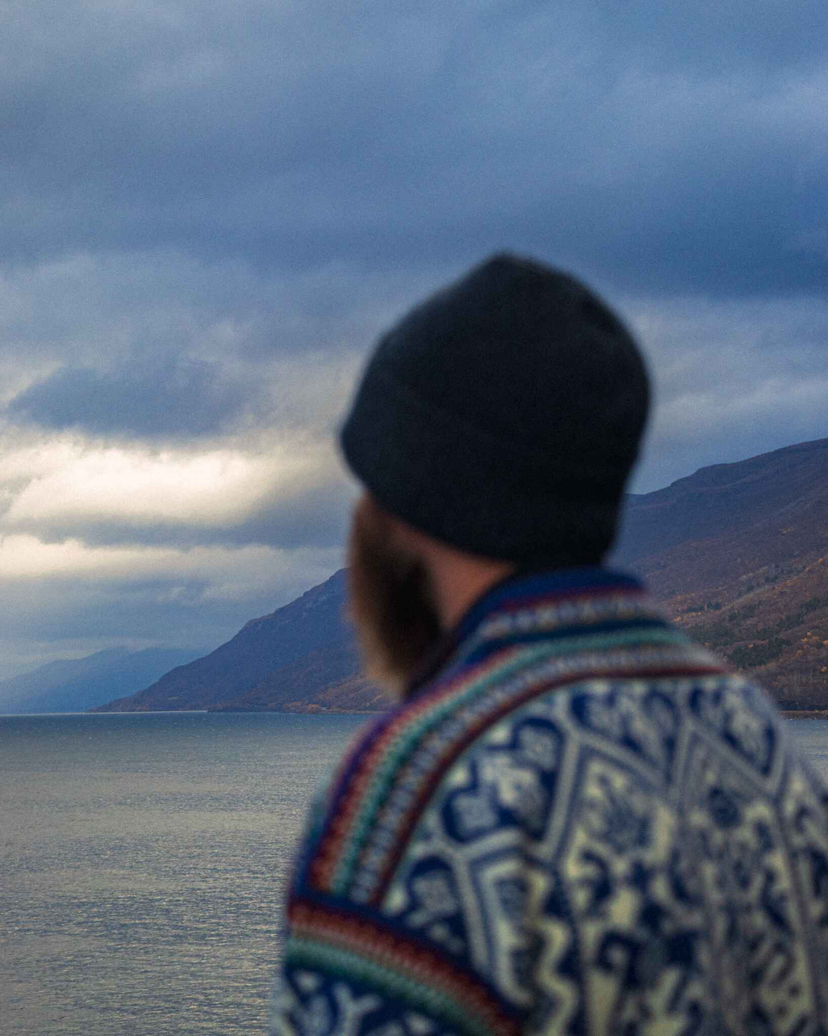 image of a man in a Norweigian sweater standing in front of a moody fjord